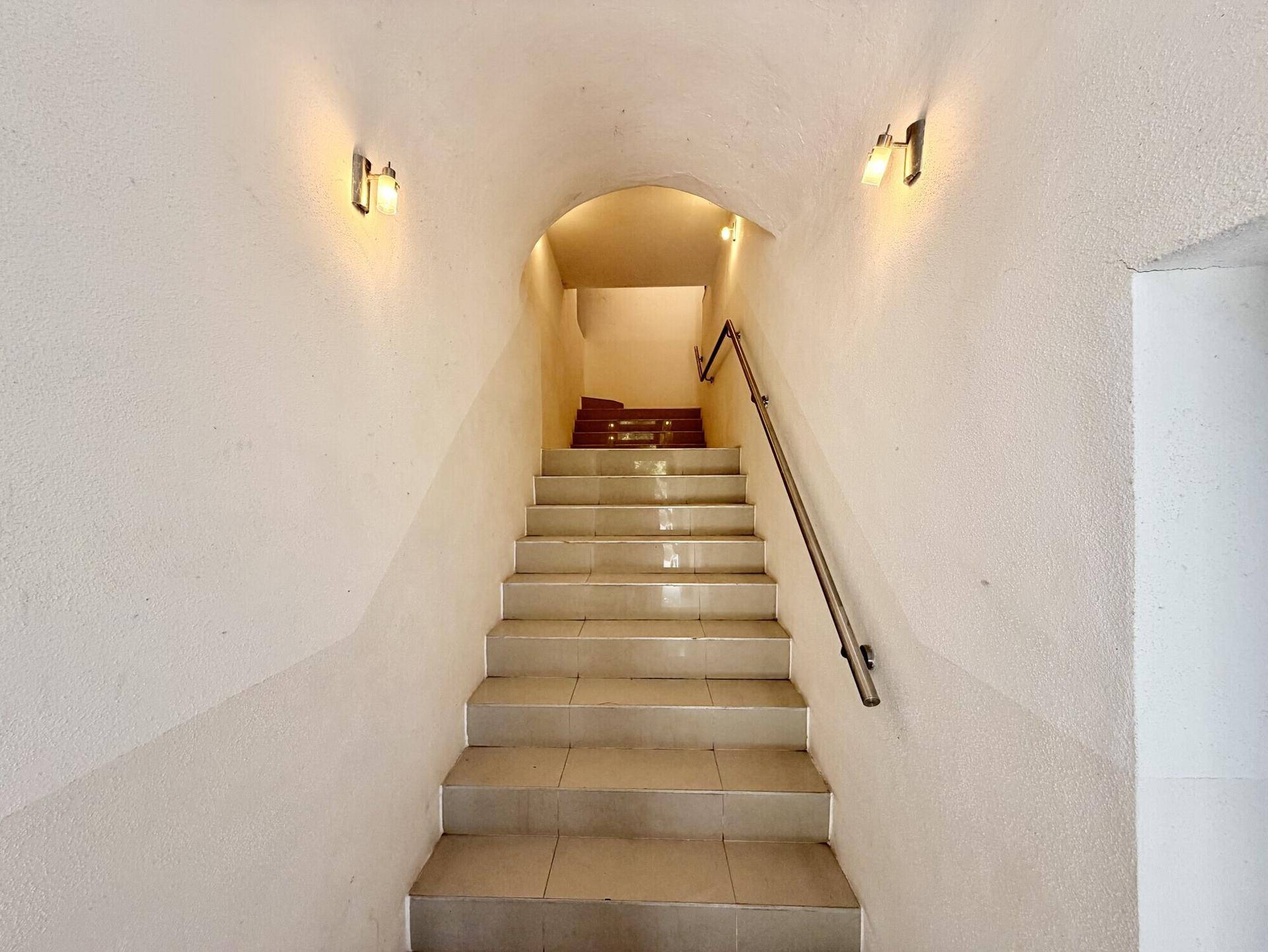 Geflieste Treppe mit Handlauf und Wandleuchten, die zu den oberen Etagen führt, unter einer Gewölbedecke.