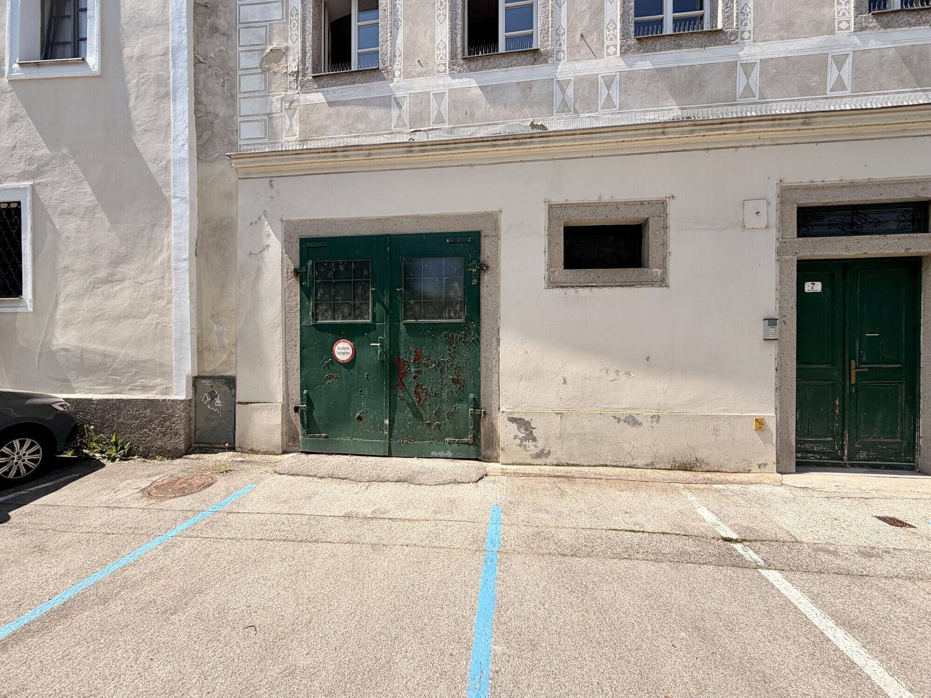 Detailansicht der historischen Gebäudefassade mit zwei markanten grünen Türen und einem Parkplatz davor.