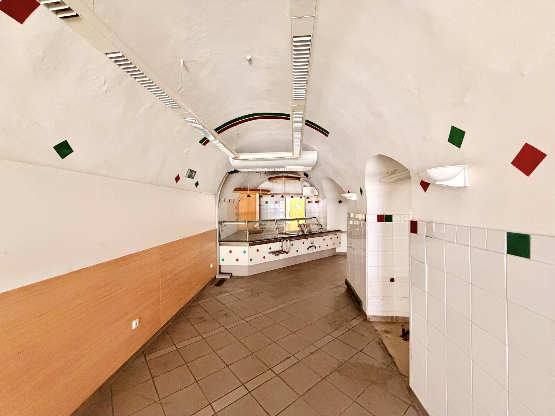 Langer Raum mit Gewölbedecken, gefliestem Boden und einer durchgehenden Theke, geeignet für Verkauf oder Gastronomie.