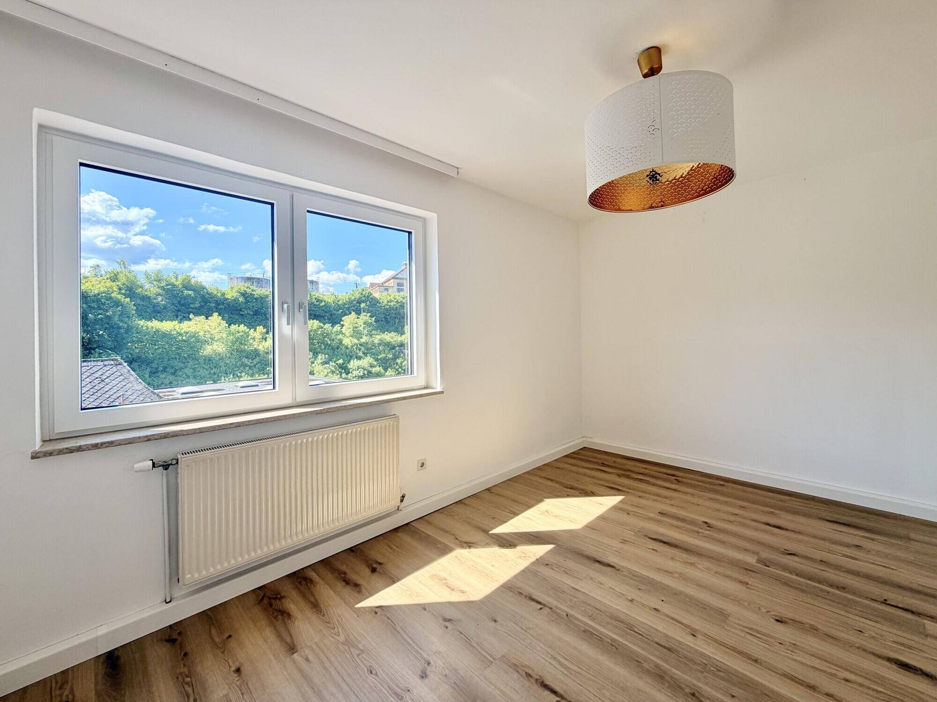 Helles Schlafzimmer mit Laminatboden, einem Fenster und moderner Deckenleuchte.