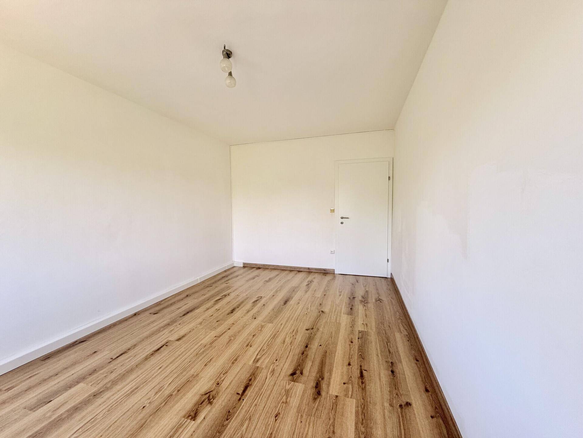 Neutral gestaltetes Zimmer mit Laminatboden und weißer Tür, bereit zur individuellen Einrichtung.