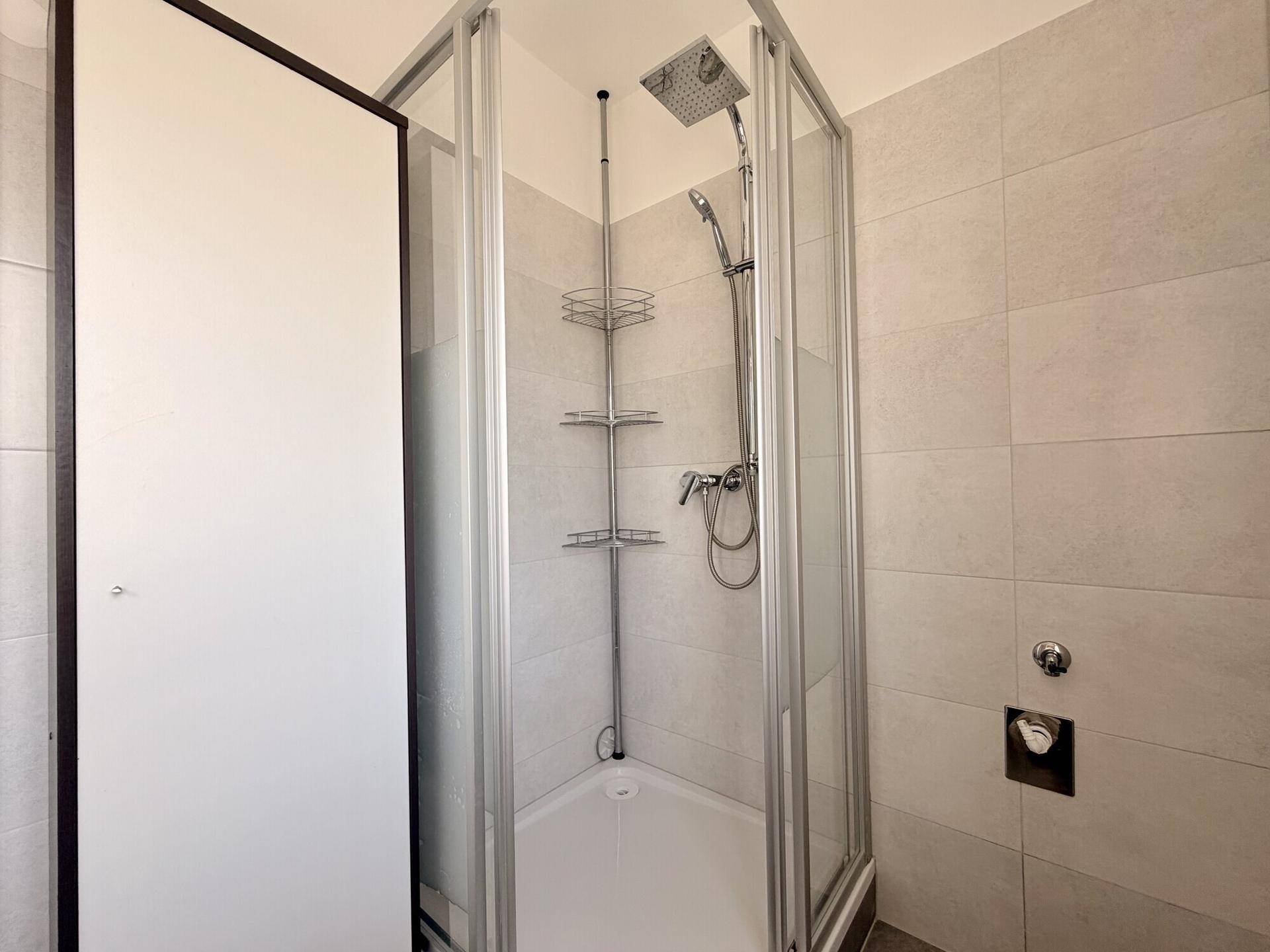 Duschkabine mit Glaswänden, Regendusche und modernen hellgrauen Wandfliesen.