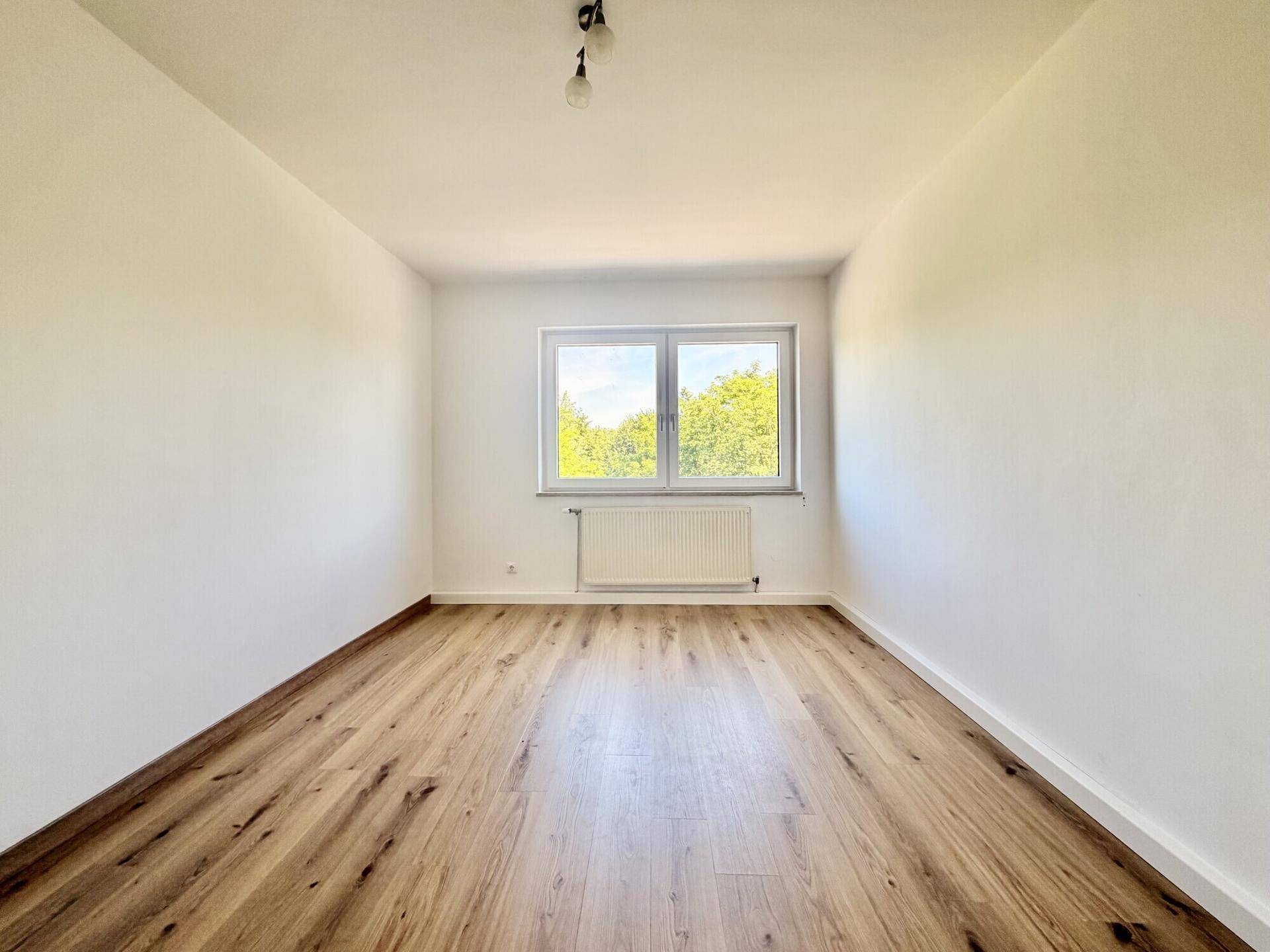 Gemütliches Zimmer mit Laminatboden und einem Fenster, das viel Tageslicht hereinlässt.