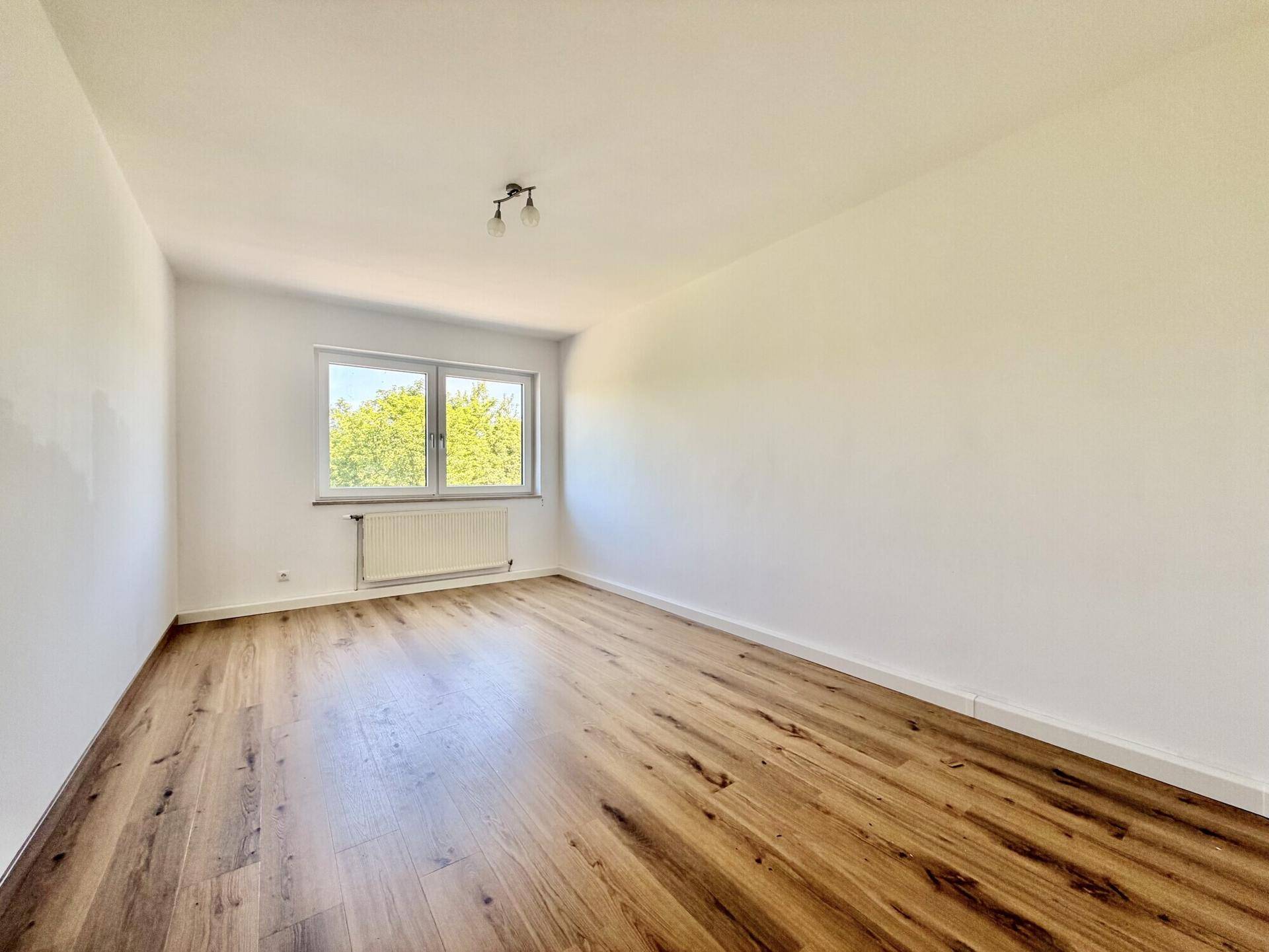 Ruhiges Schlafzimmer mit Laminatboden, weißen Wänden und Blick ins Grüne.