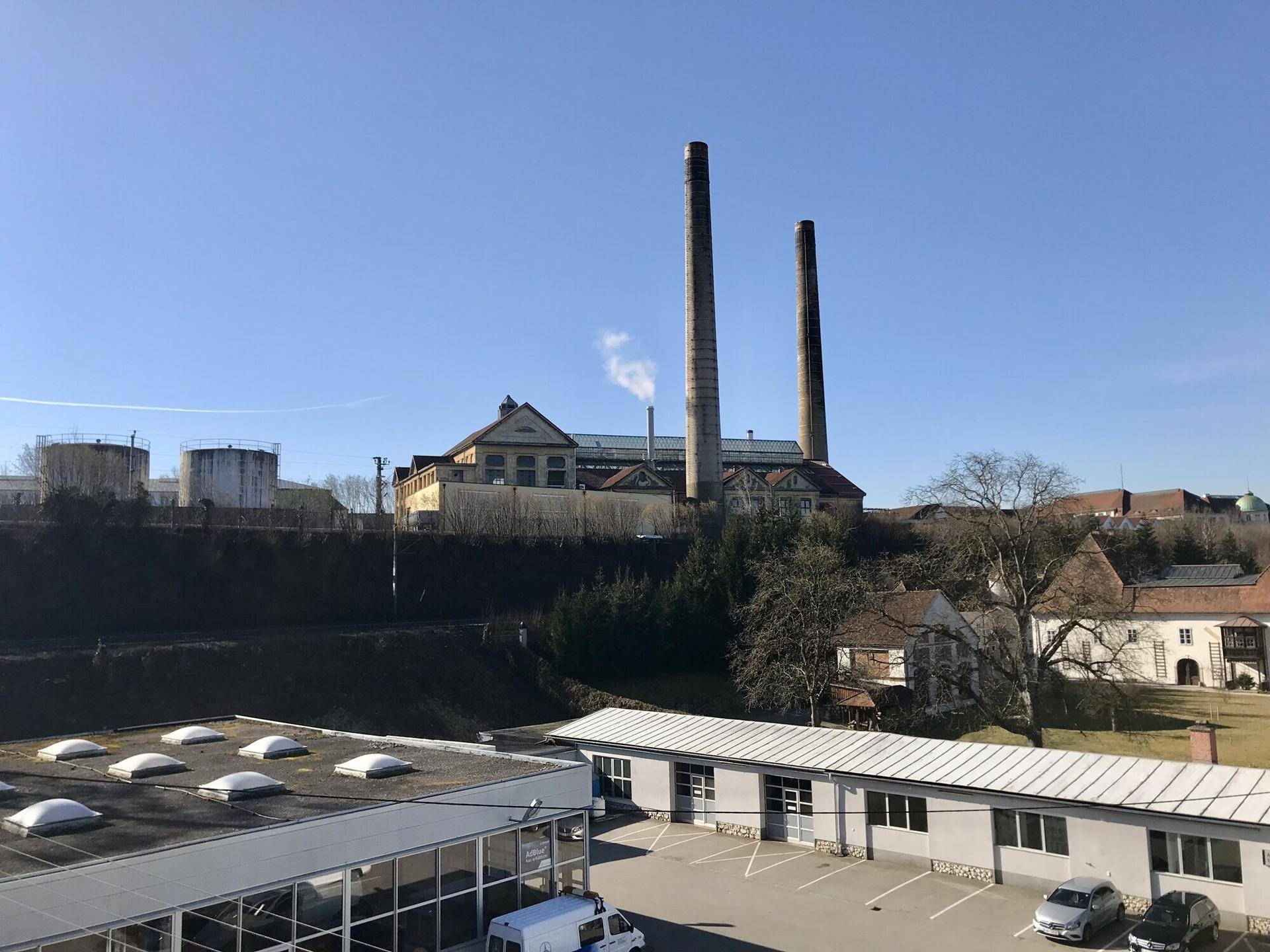 Weitläufiger Blick auf eine Industrieanlage mit hohen Schornsteinen und umliegende Gebäude.