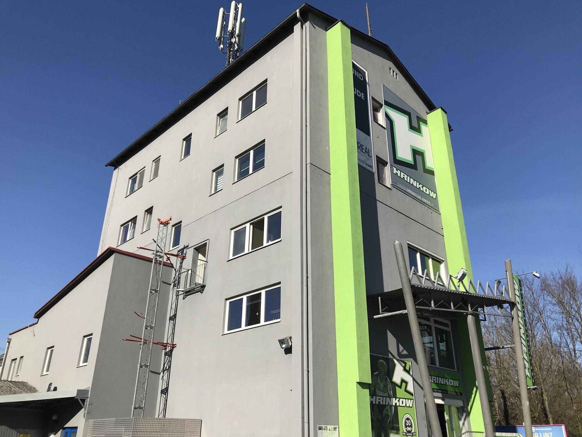Mehrstöckiges Gebäude mit moderner grauer Fassade und auffälligen grünen Akzenten.