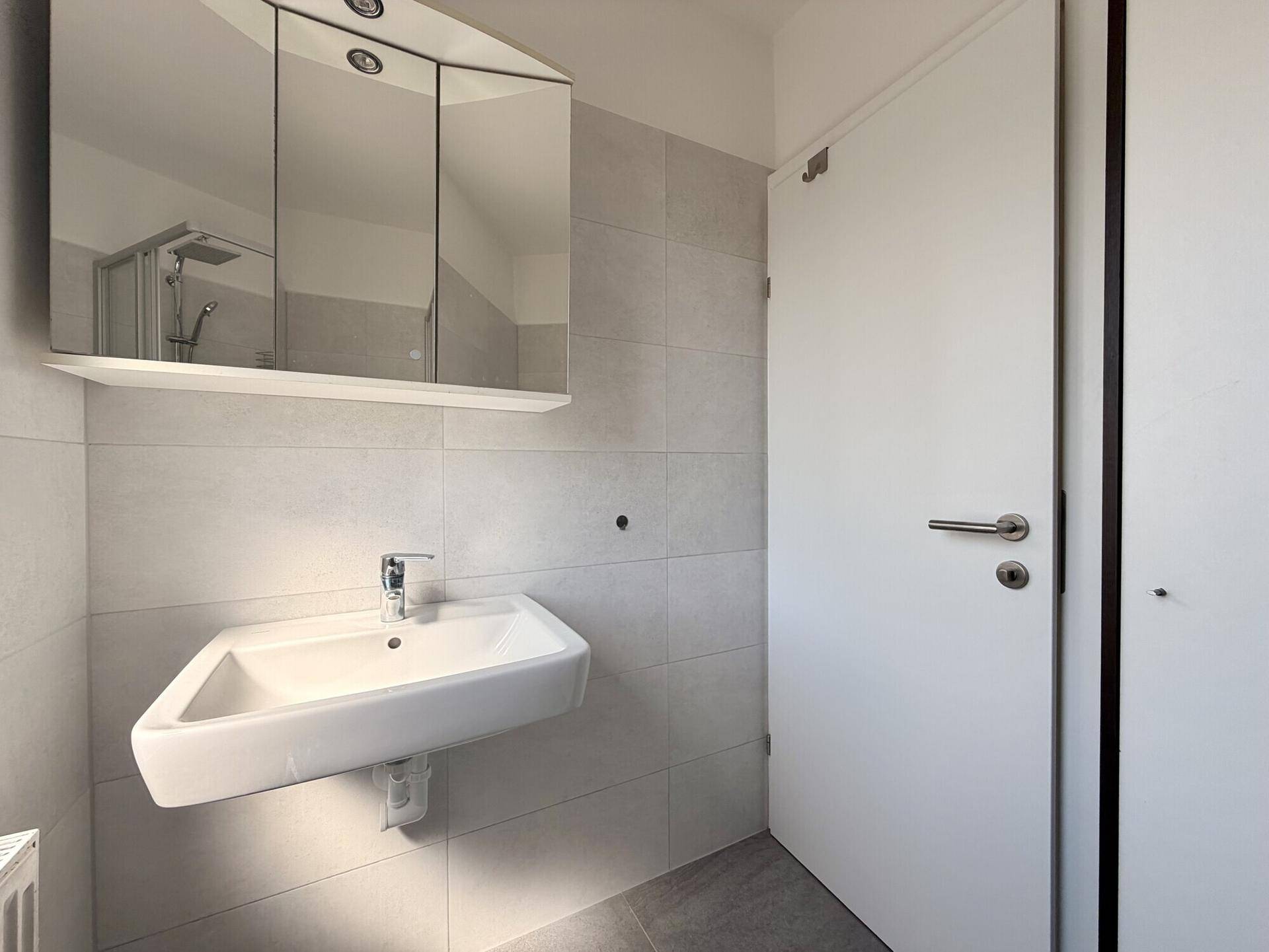 Modernes Badezimmer mit Waschbecken, Spiegelschrank und hellgrauen Fliesen.