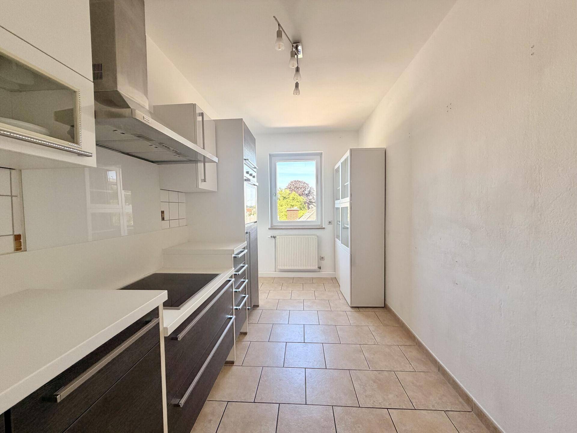 Funktionale Küche mit Fliesenboden, Fenster und ausreichend Stauraum in den Schränken.
