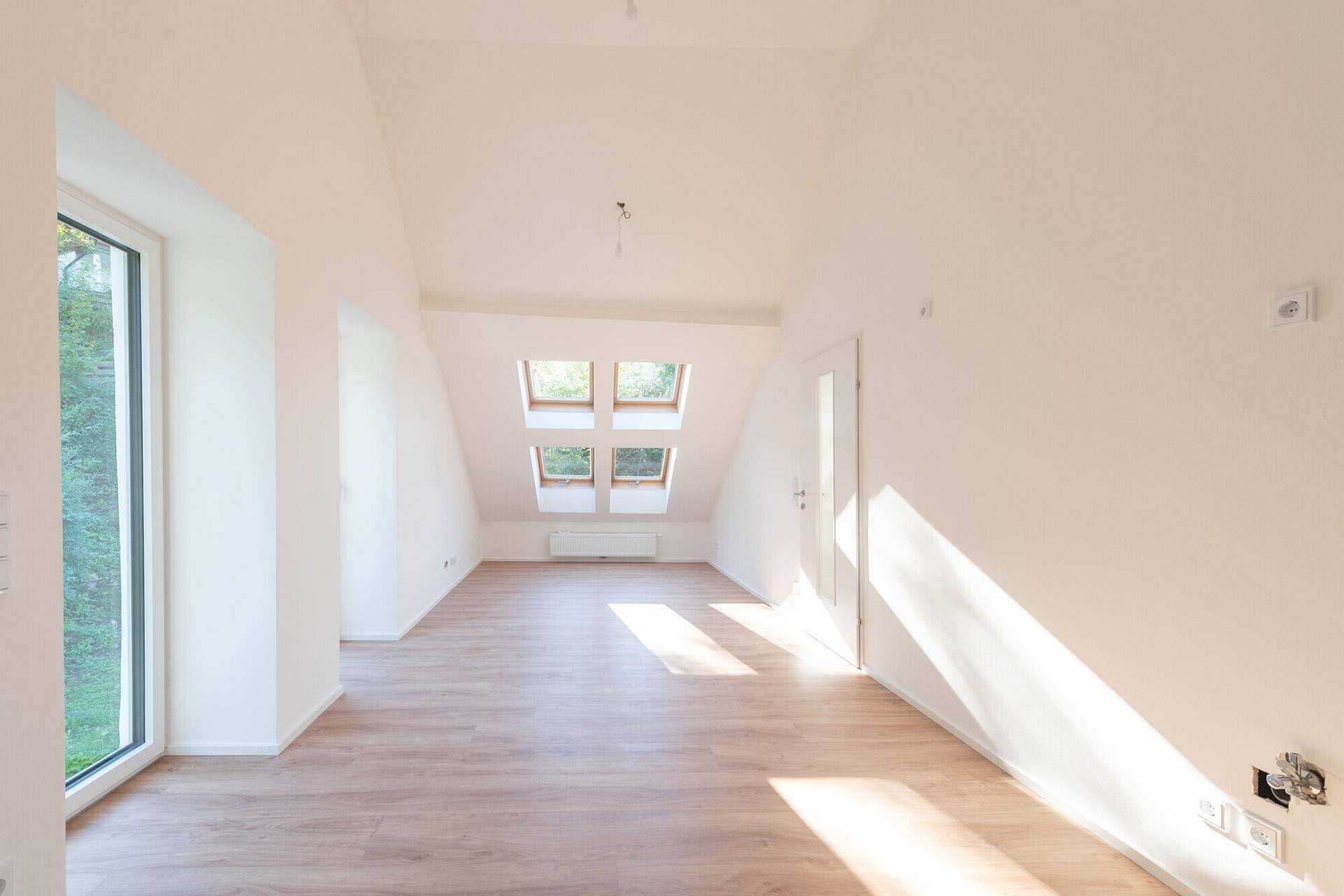 Heller Raum im Dachgeschoss mit großen Fenstern, Laminatboden und viel Sonneneinstrahlung.