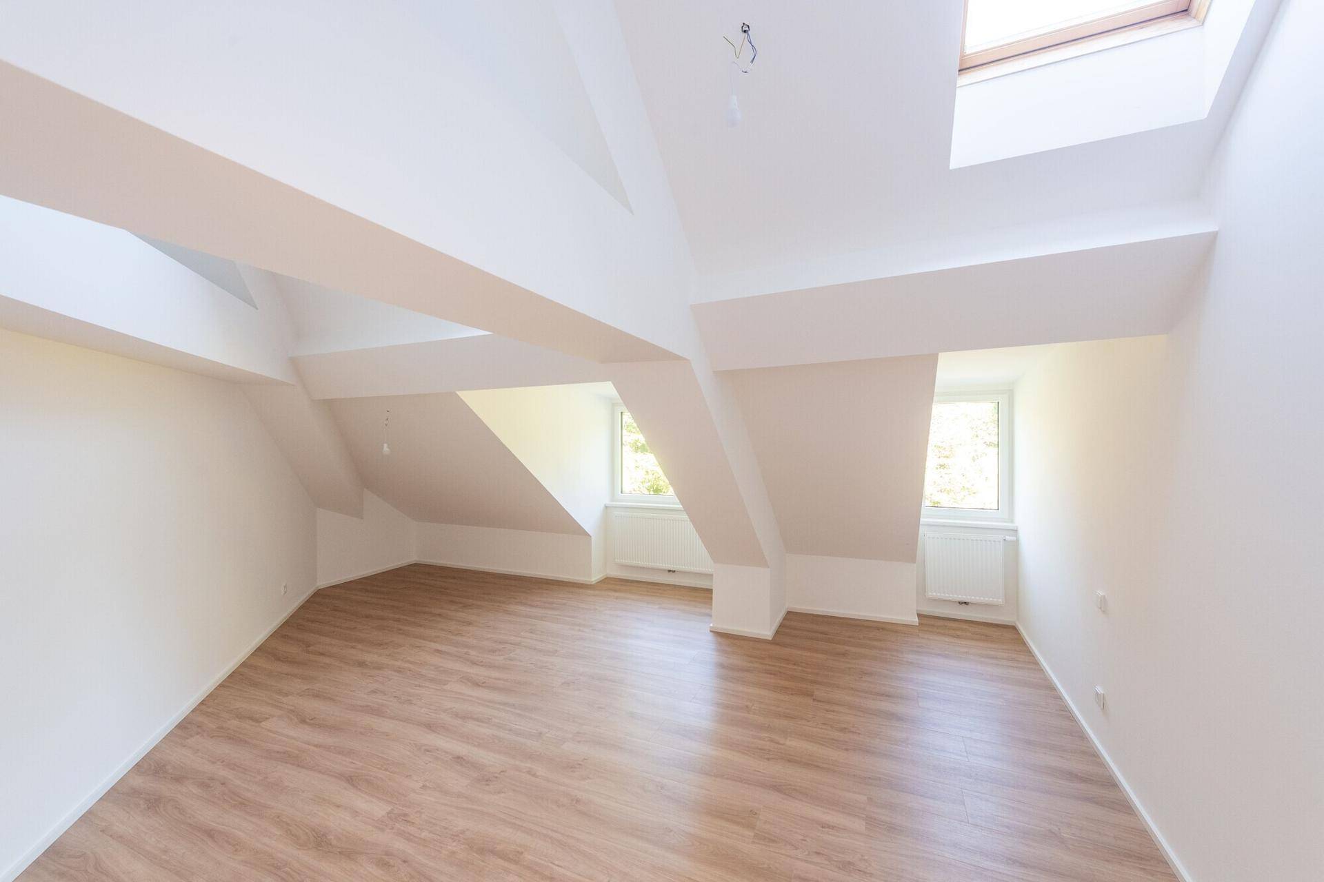 Heller Dachbodenraum mit Laminatboden, schrägen Wänden und Dachfenstern für viel Tageslicht.