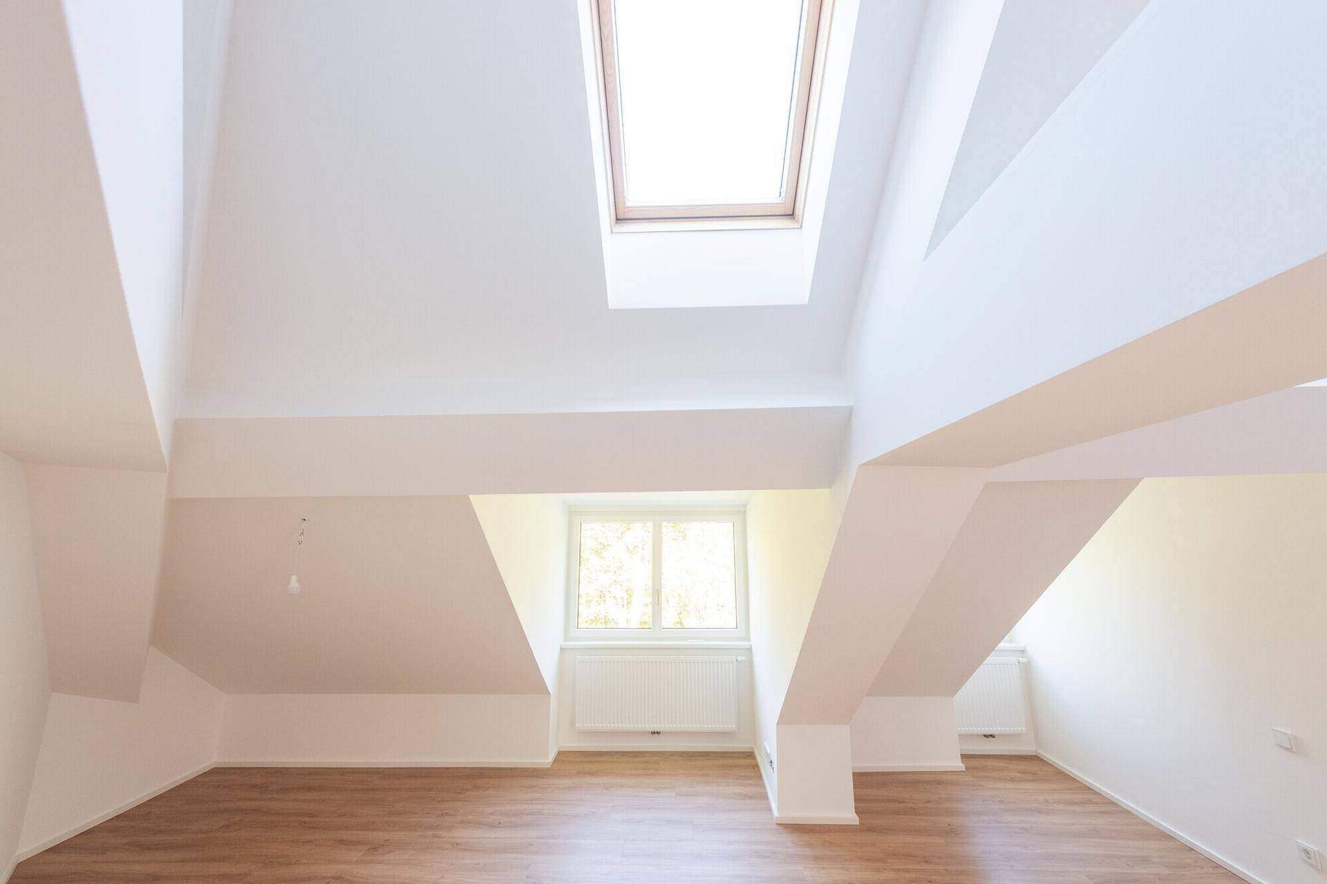 Geräumiger Dachbodenraum mit Holzbalken, Laminatboden und viel Tageslicht durch Dachfenster.