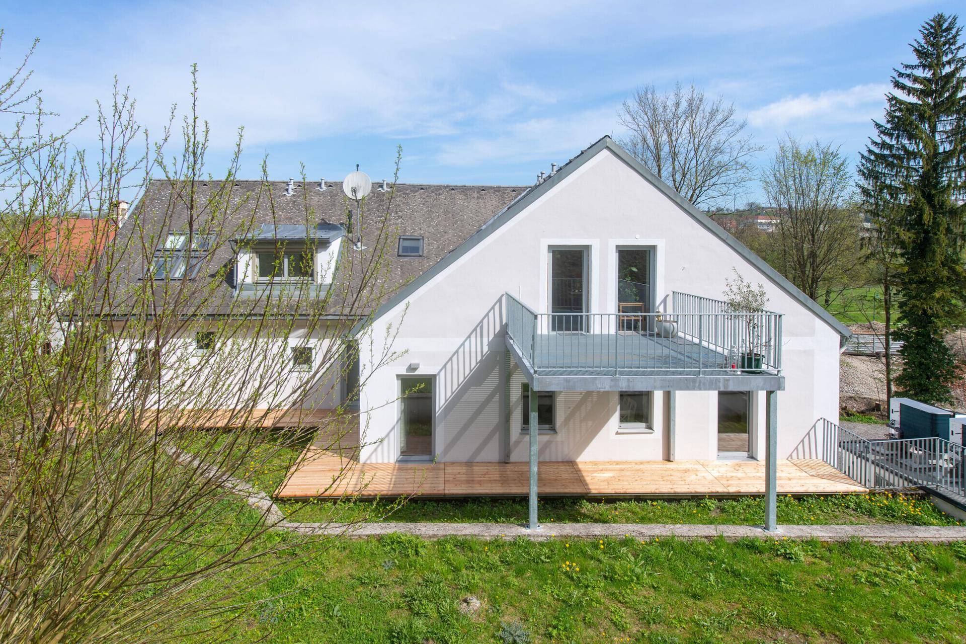 Rückansicht des Hauses mit großem Balkon und Holzterrasse, umgeben von grüner Natur.