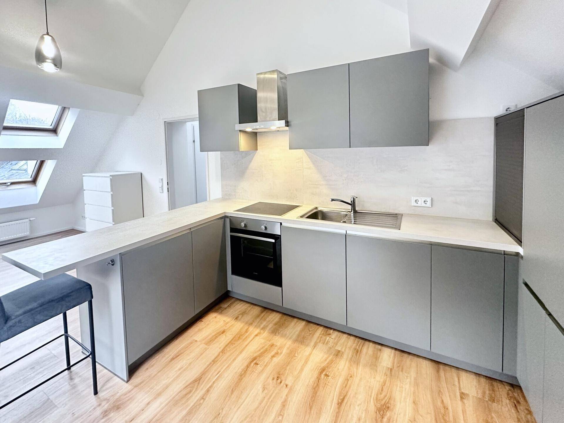 Moderne Einbauküche in Grau mit Kochinsel, integrierten Geräten und Dachfenstern.