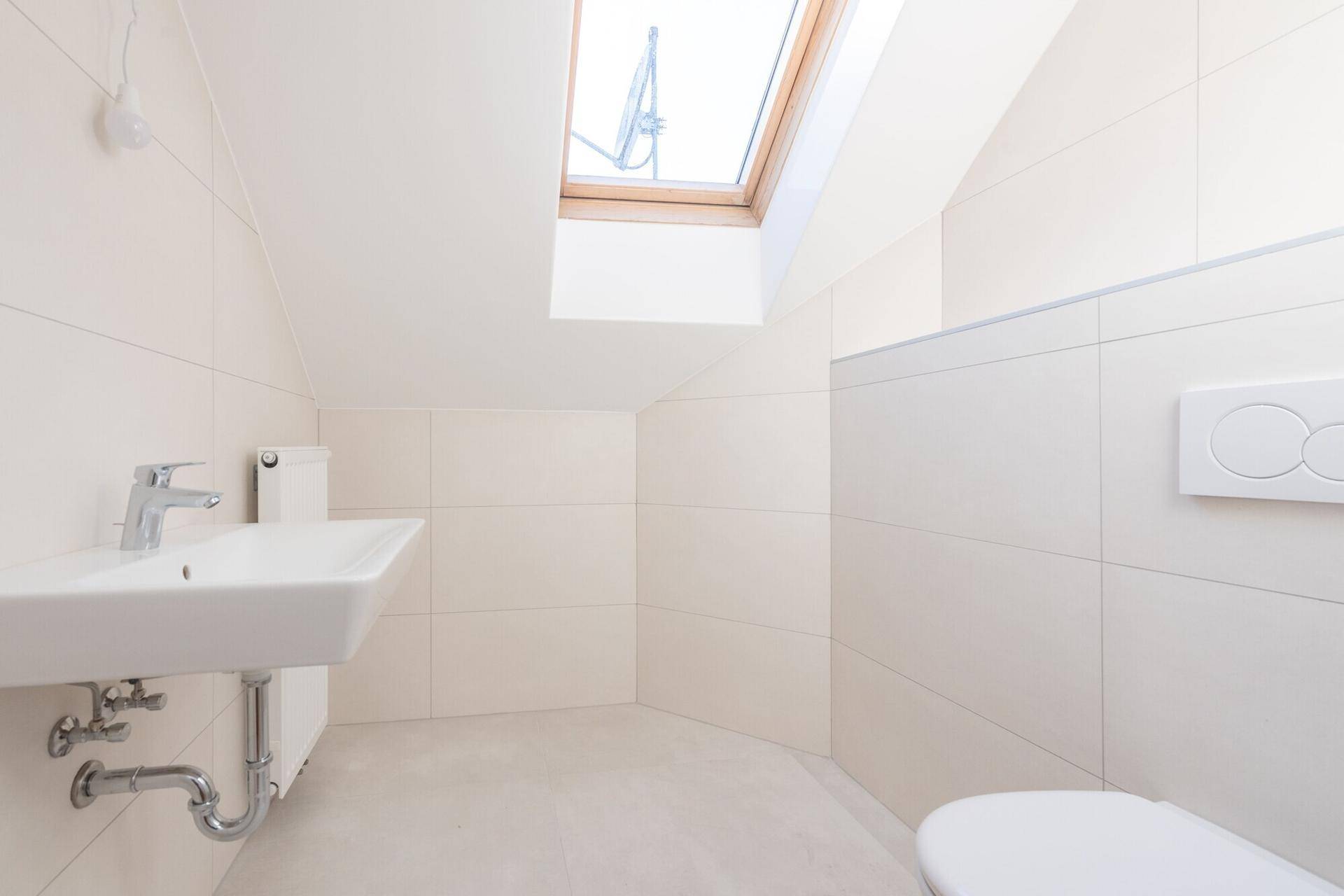 Modernes WC mit Waschbecken, wandhängender Toilette und Dachfenster für Helligkeit.