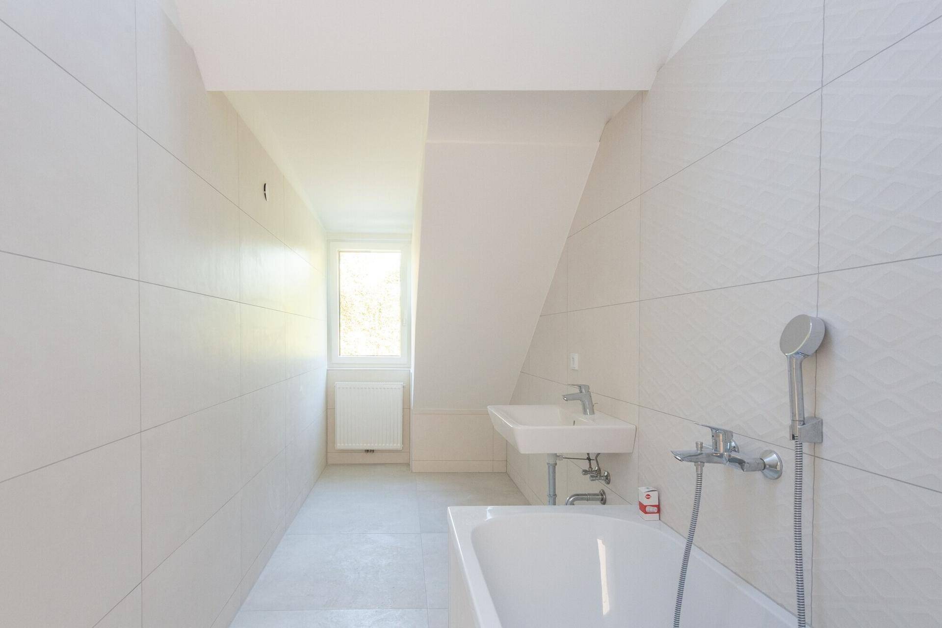 Helles Badezimmer mit Badewanne, Waschbecken, Fliesen und Fenster für Tageslicht.