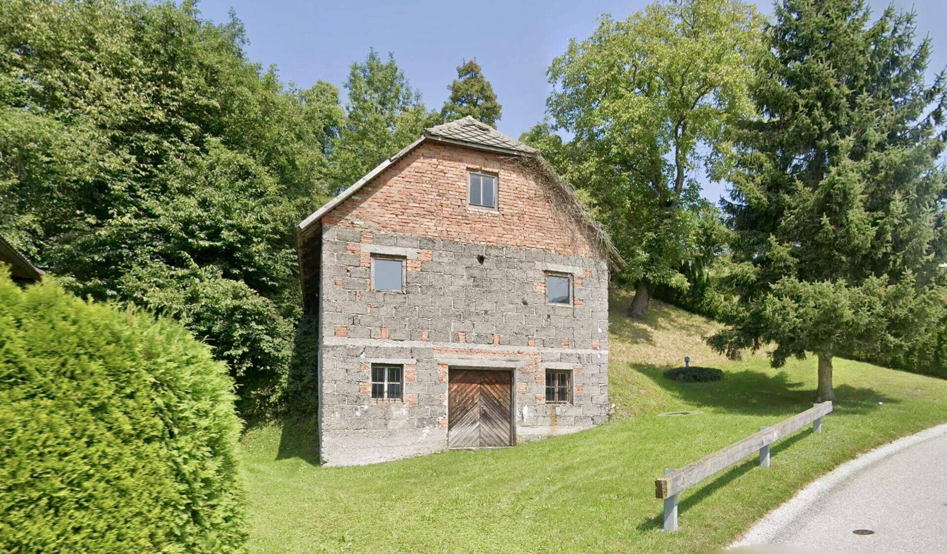 Altes, rustikales Gebäude aus Stein und Ziegeln auf einem grünen Hügel mit Bäumen.