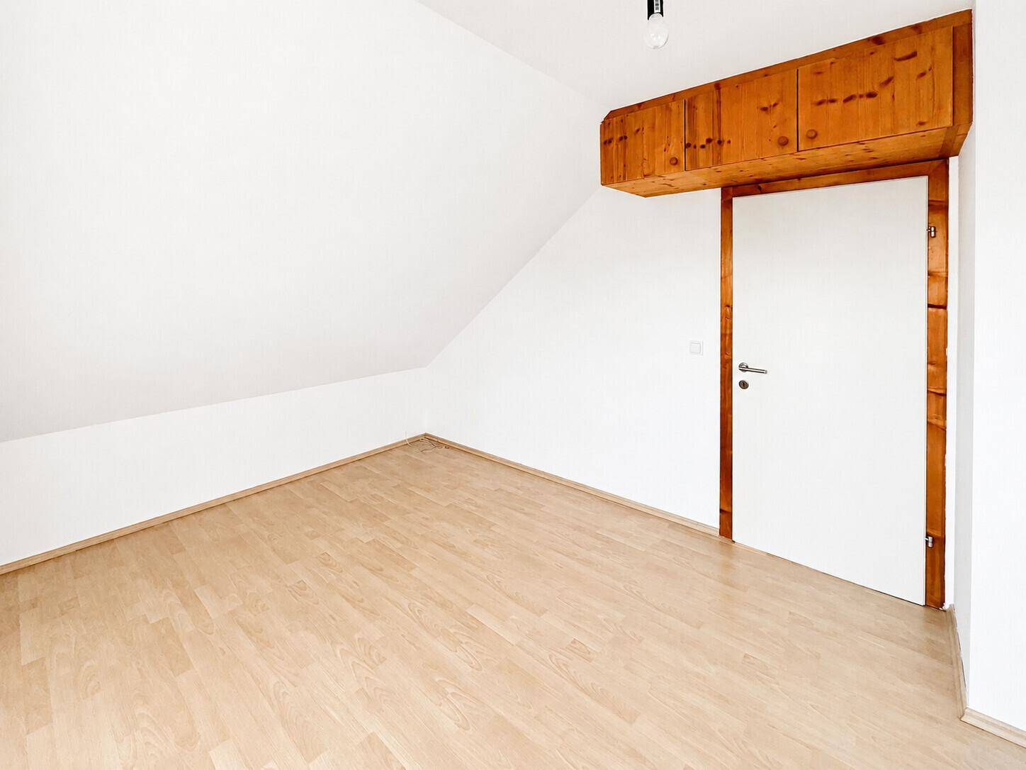 Dachgeschosszimmer mit Laminatboden, Holzeinbauten über der Tür und weißer Wandfarbe.