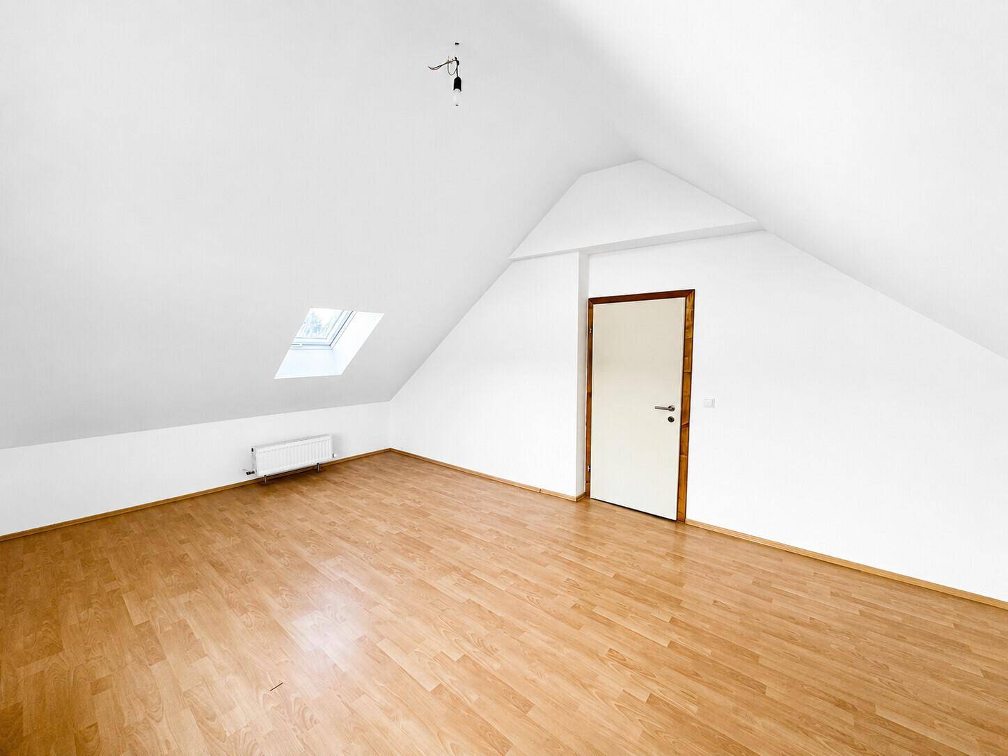 Dachgeschosszimmer mit Laminatboden, Dachfenster und einer Tür mit Holzrahmen.