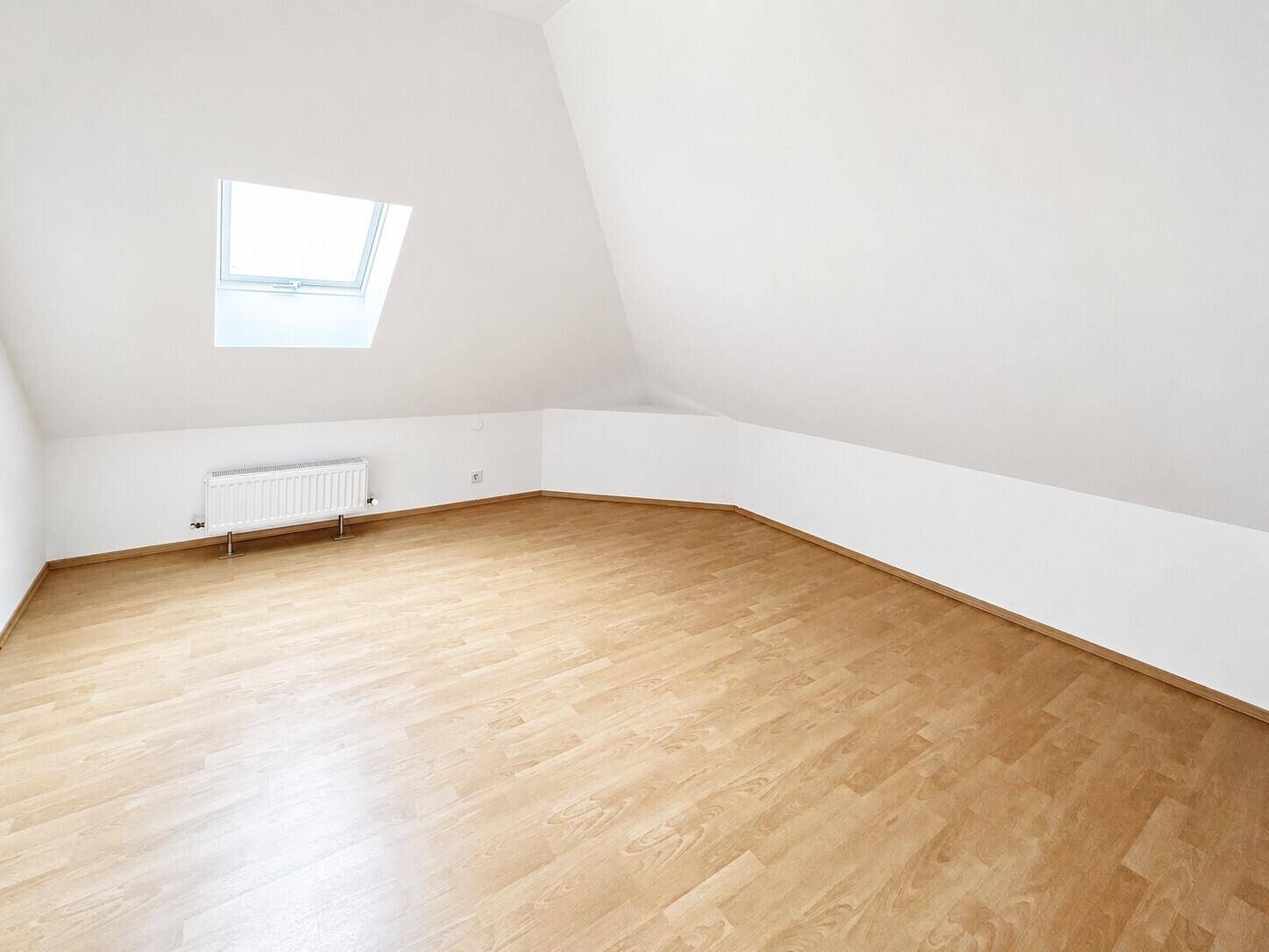 Ruhiges Dachgeschosszimmer mit Laminatboden, Dachfenster und weiß gestrichenen Wänden.