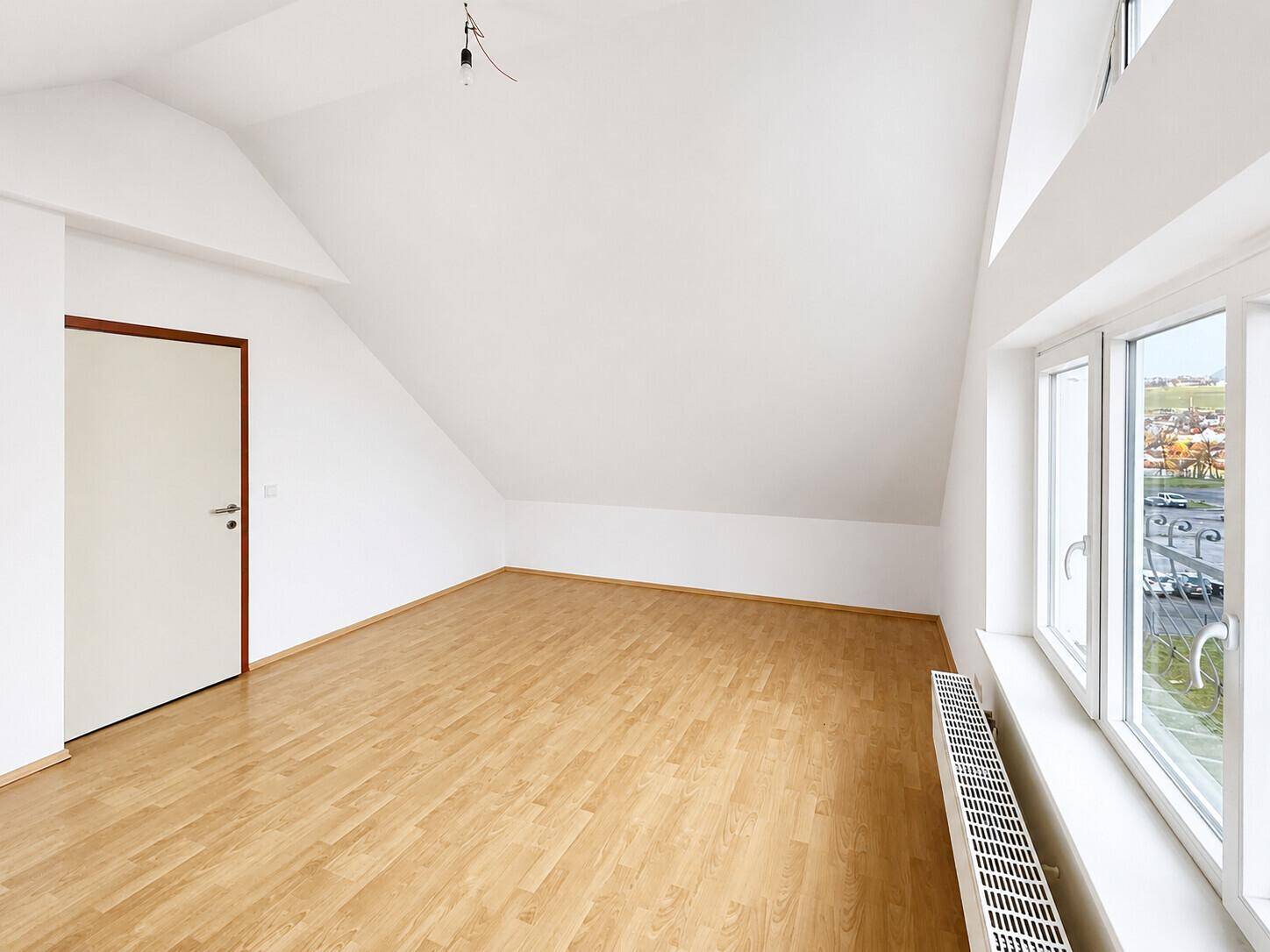 Helles Dachgeschosszimmer mit Laminatboden, schrägen Wänden und einem Fenster mit Ausblick.