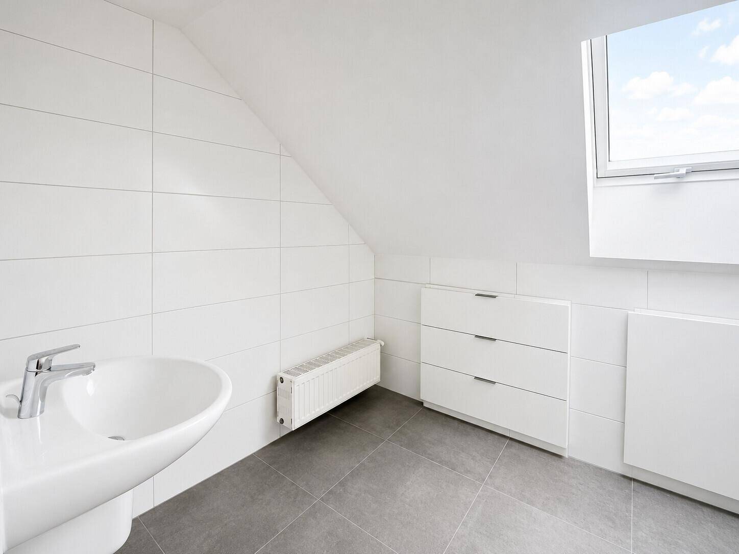 Helles Badezimmer mit Waschbecken, Dachfenster und weißen Fliesen im Dachgeschoss.
