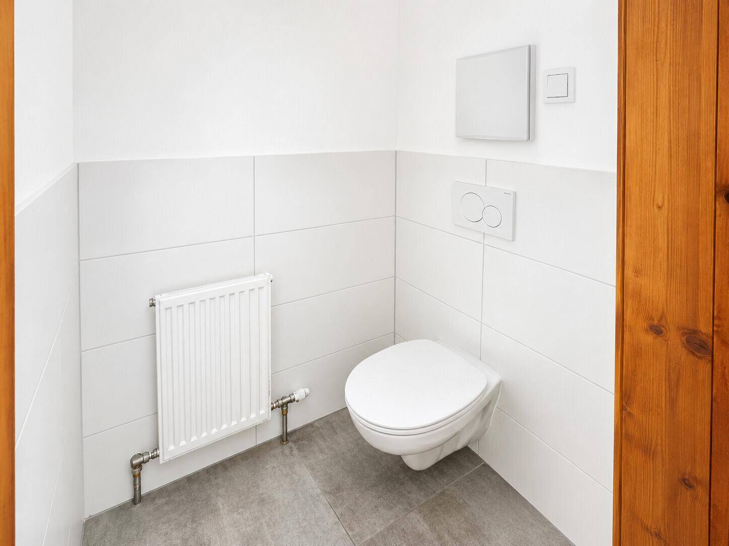 Separates WC mit wandhängender Toilette, Heizkörper und weißen Wandfliesen.