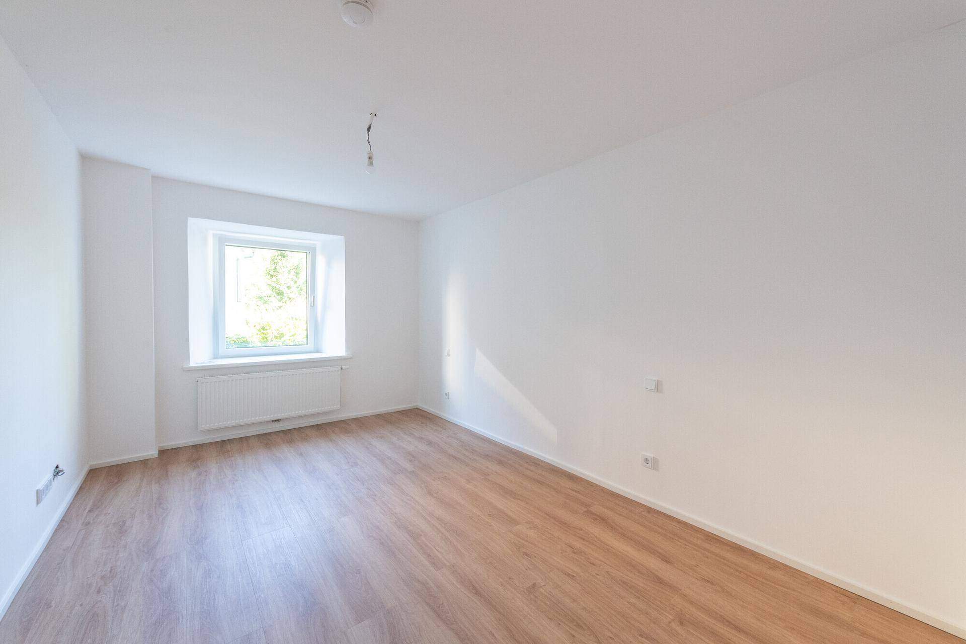 Ruhiges Schlafzimmer mit hellem Laminatboden und einem Fenster, bietet viel natürliches Licht.