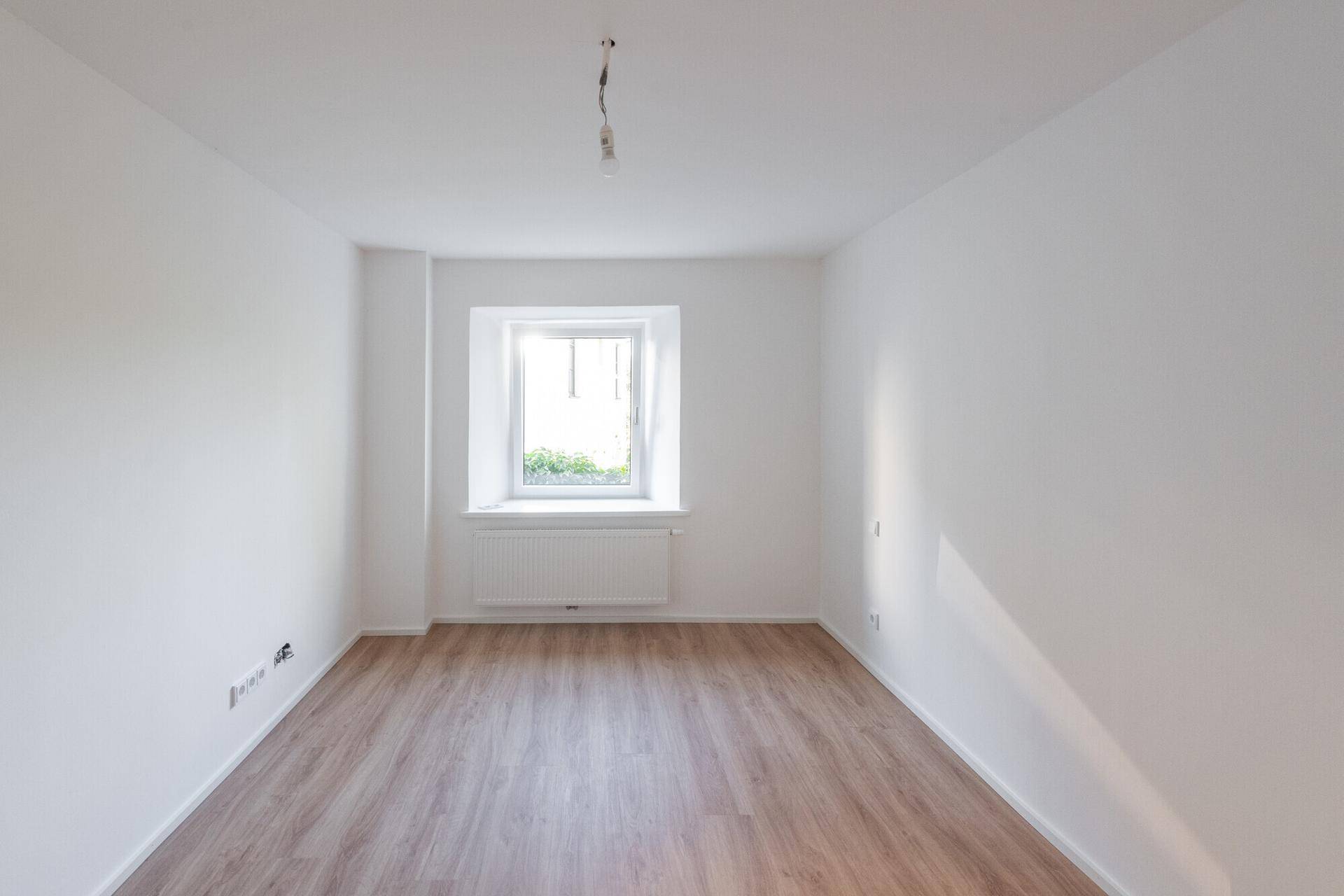 Helles Zimmer mit Laminatboden und einem Fenster, bietet eine angenehme Atmosphäre zum Entspannen.