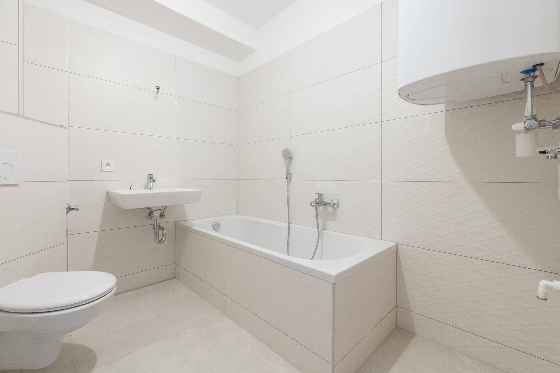 Modernes Badezimmer mit weißen Fliesen, Badewanne, WC und Waschbecken, ausgestattet mit Warmwasserboiler.