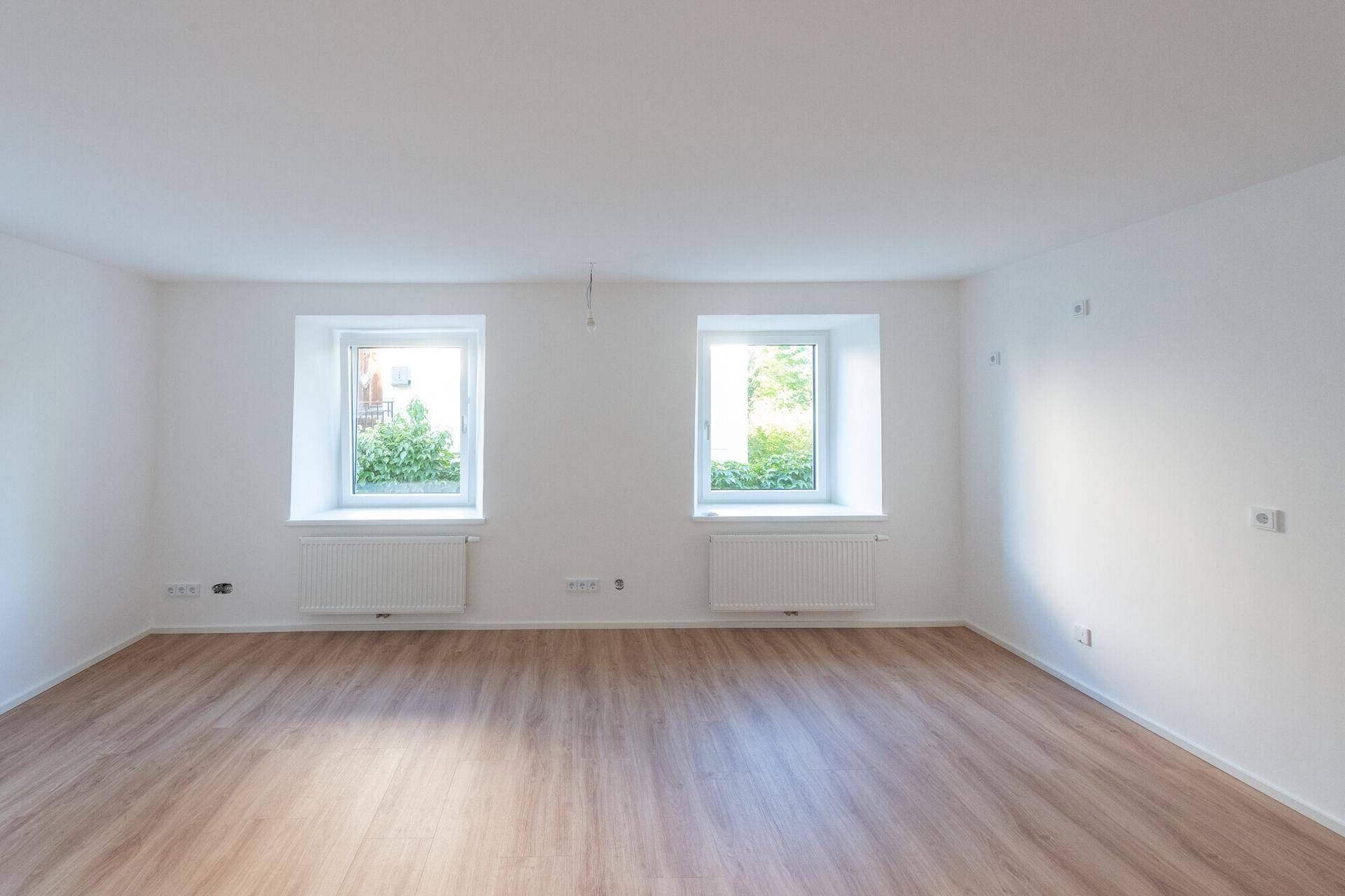 Geräumiges, helles Zimmer mit Laminatboden und zwei Fenstern, ideal als Schlaf- oder Wohnbereich.