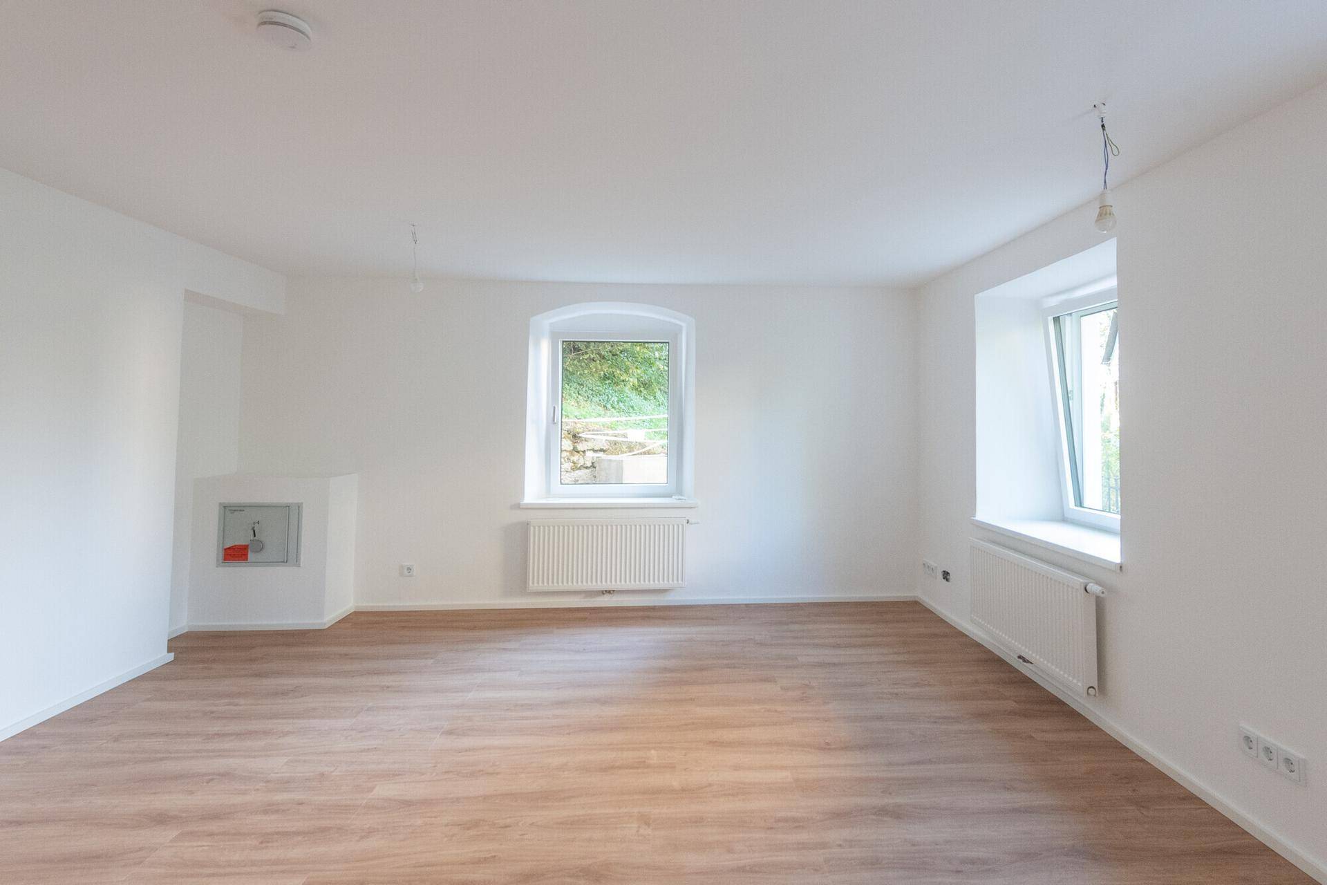Heller Wohnraum mit Laminatboden, zwei Fenstern und einer Nische, ideal für einen Kamin.