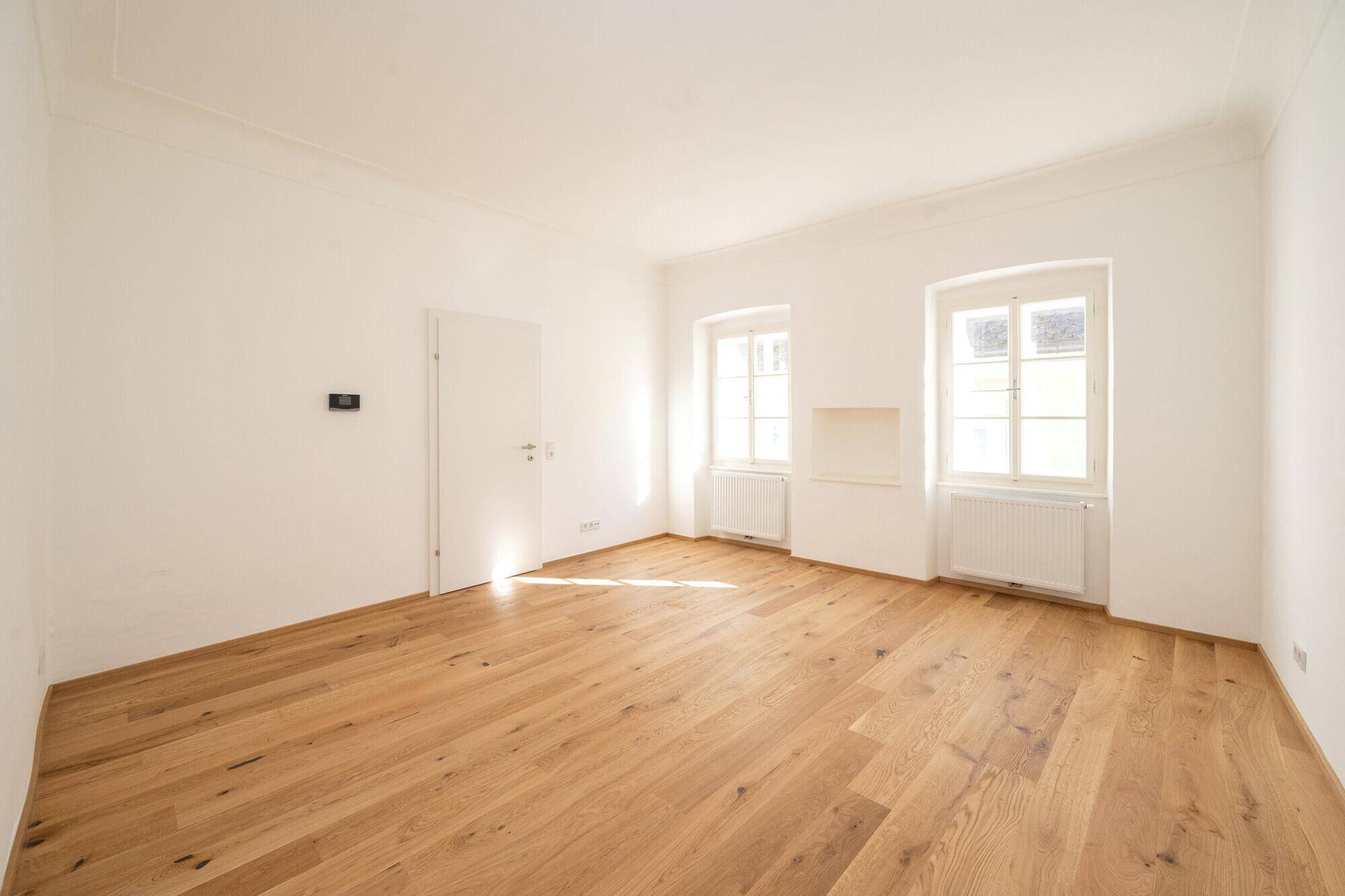 Renoviertes Zimmer mit Holzboden und zwei Fenstern, bietet vielseitige Nutzungsmöglichkeiten.