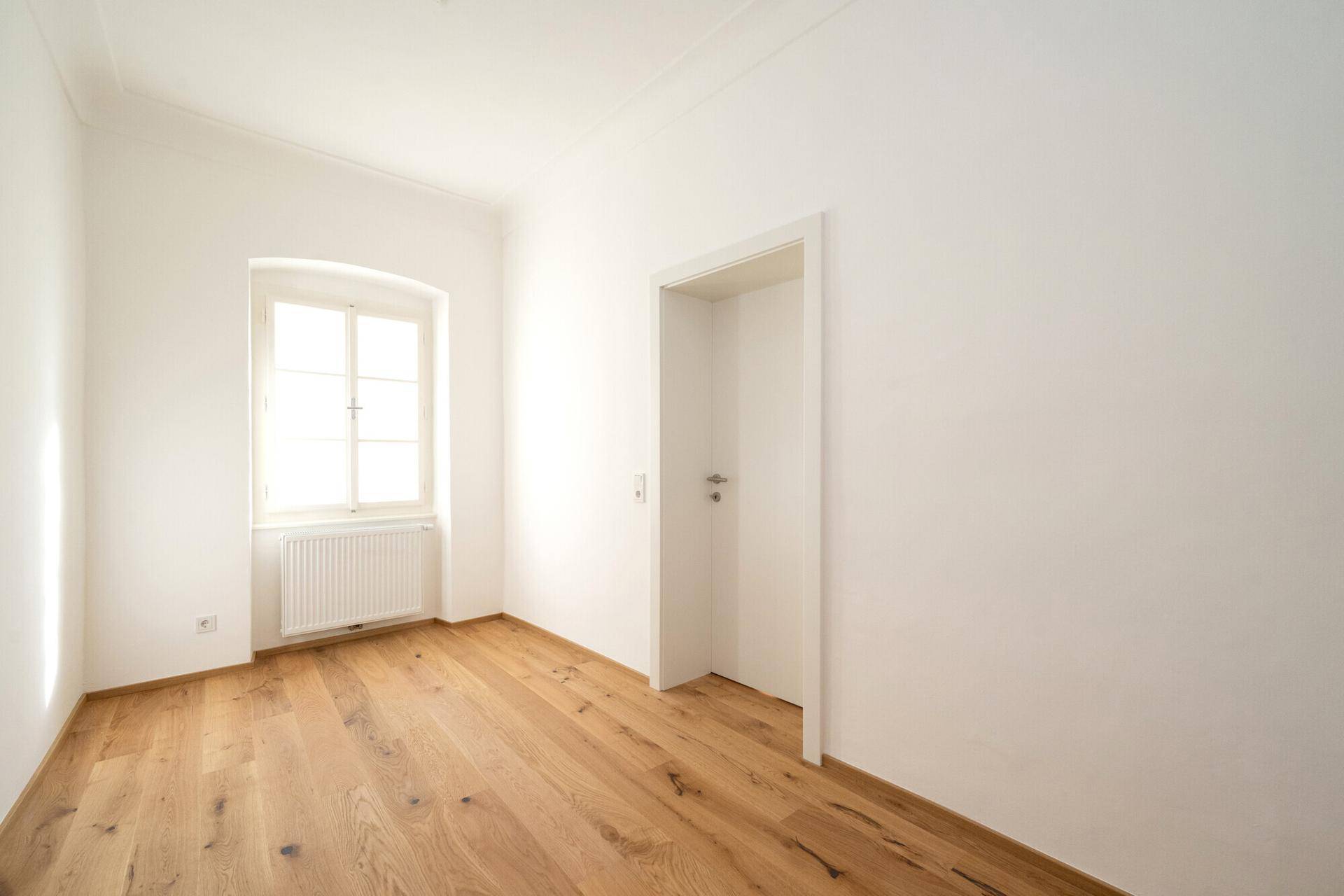 Gemütliches Zimmer mit Holzboden und einem Fenster, ideal als Schlaf- oder Arbeitszimmer.