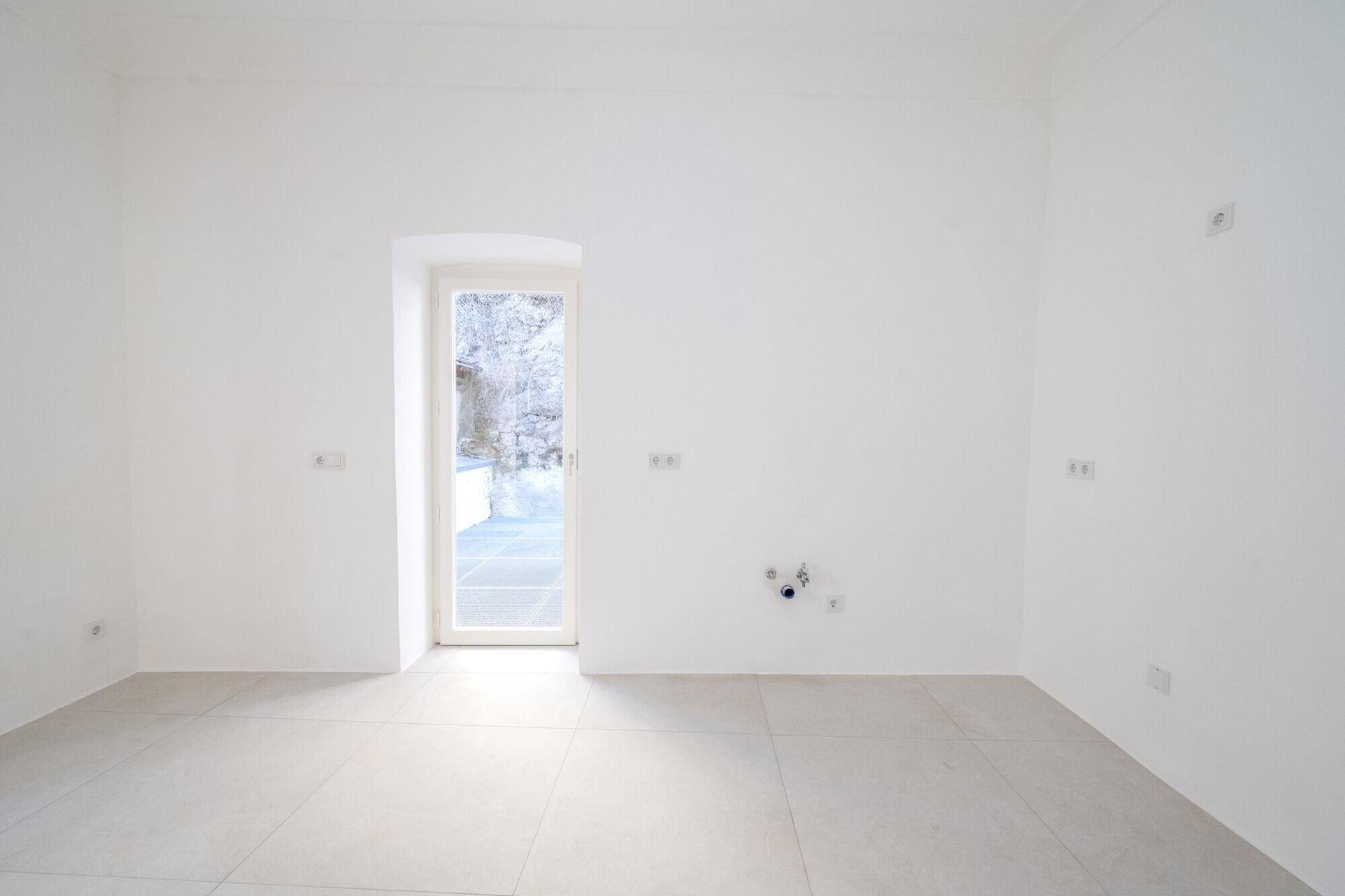 Heller Raum mit Fliesenboden und Zugang nach draußen, vorbereitet für Installationen.
