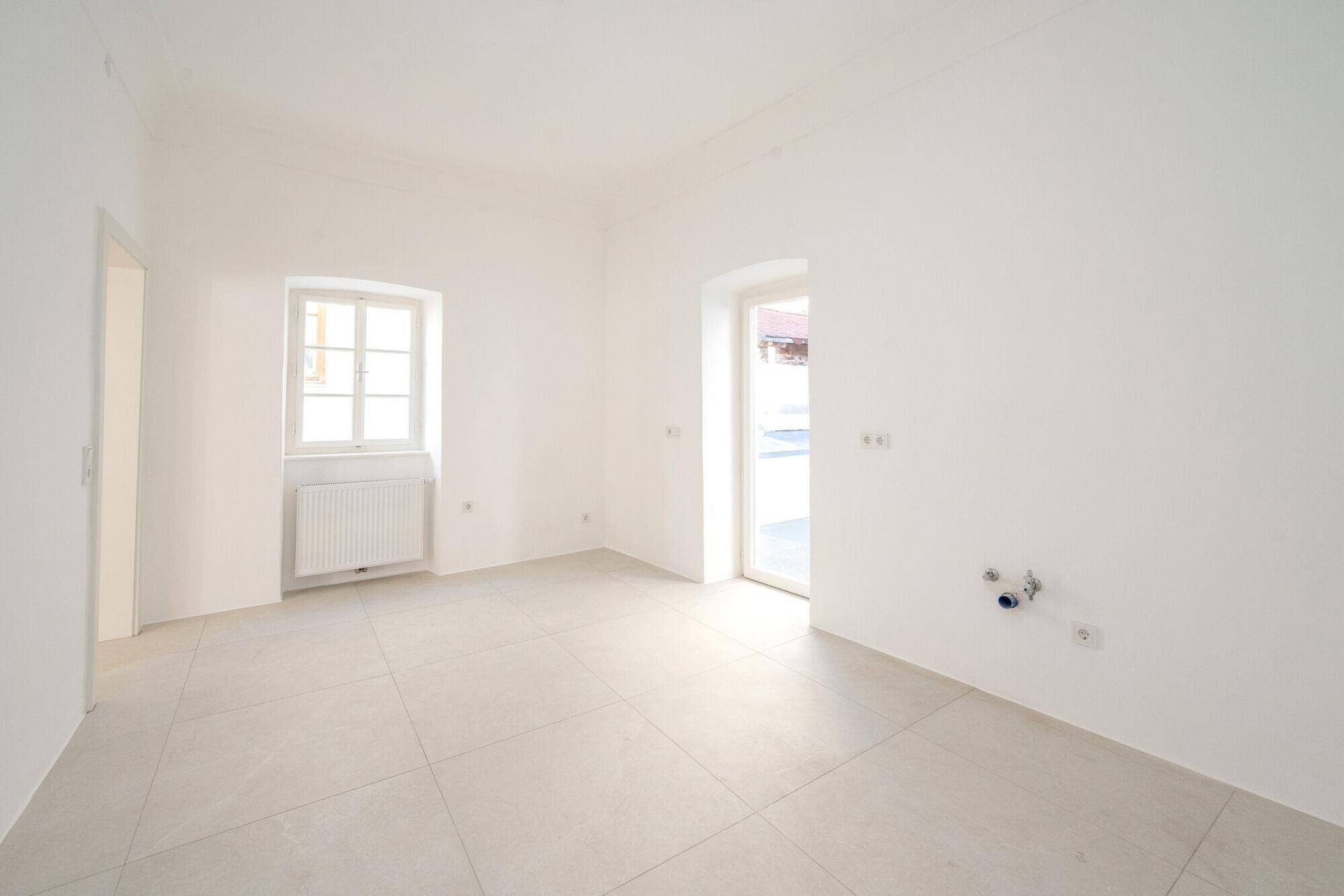Renovierter Raum mit Fliesenboden und Fenster, vorbereitet für Küchen- oder Badinstallationen.