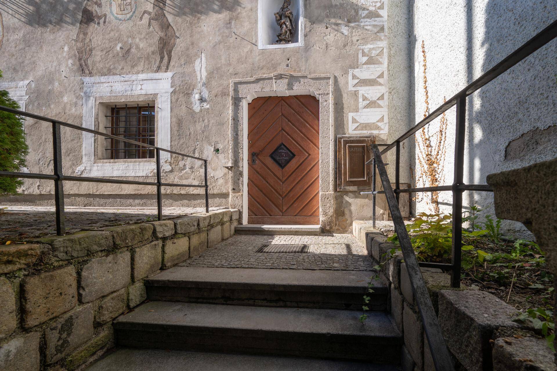 Historischer Eingangsbereich mit Holztür, Steintreppe und dekorativen Wandmalereien.