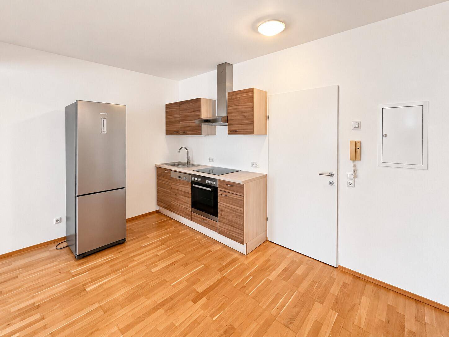 Moderne Küchenzeile mit Holzfronten, integrierten Geräten und einem freistehenden Kühlschrank.
