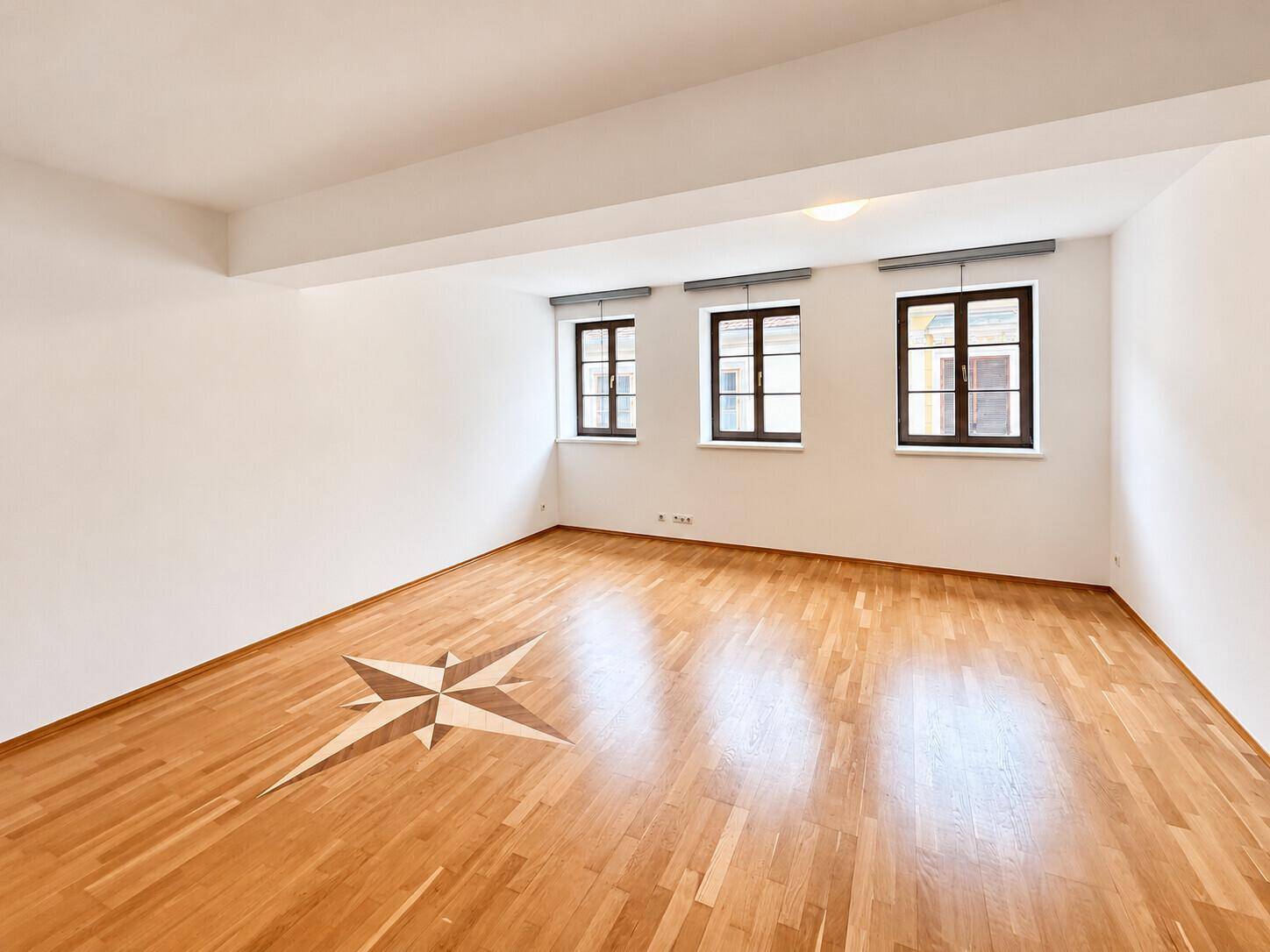 Helles Wohnzimmer mit Parkettboden und dekorativem Sternmotiv, bietet viel Platz für Möbel und Einrichtung.