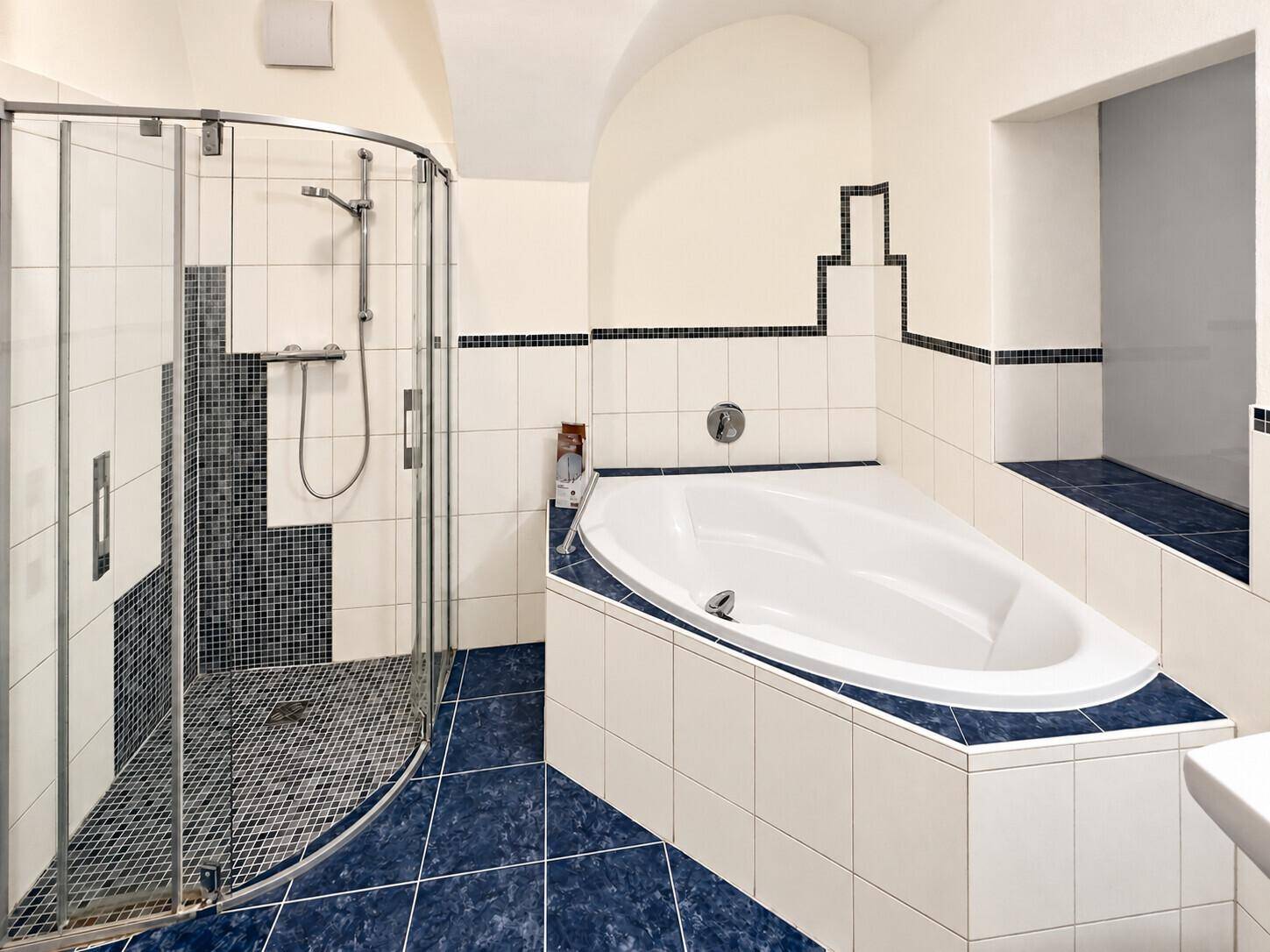 Geräumiges Badezimmer mit Badewanne, Duschkabine und blauen Fliesen im Bodenbereich, hell und sauber.
