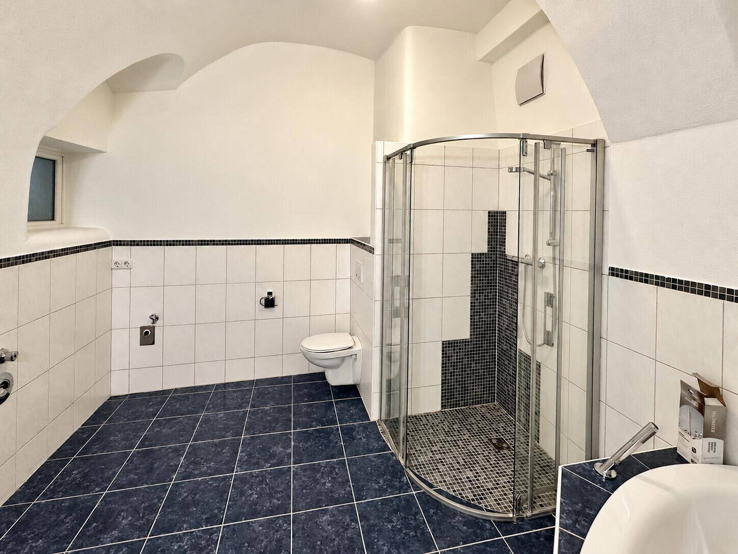 Badezimmer mit Duschkabine, Toilette und blauen Bodenfliesen, bietet ausreichend Platz und Funktionalität.