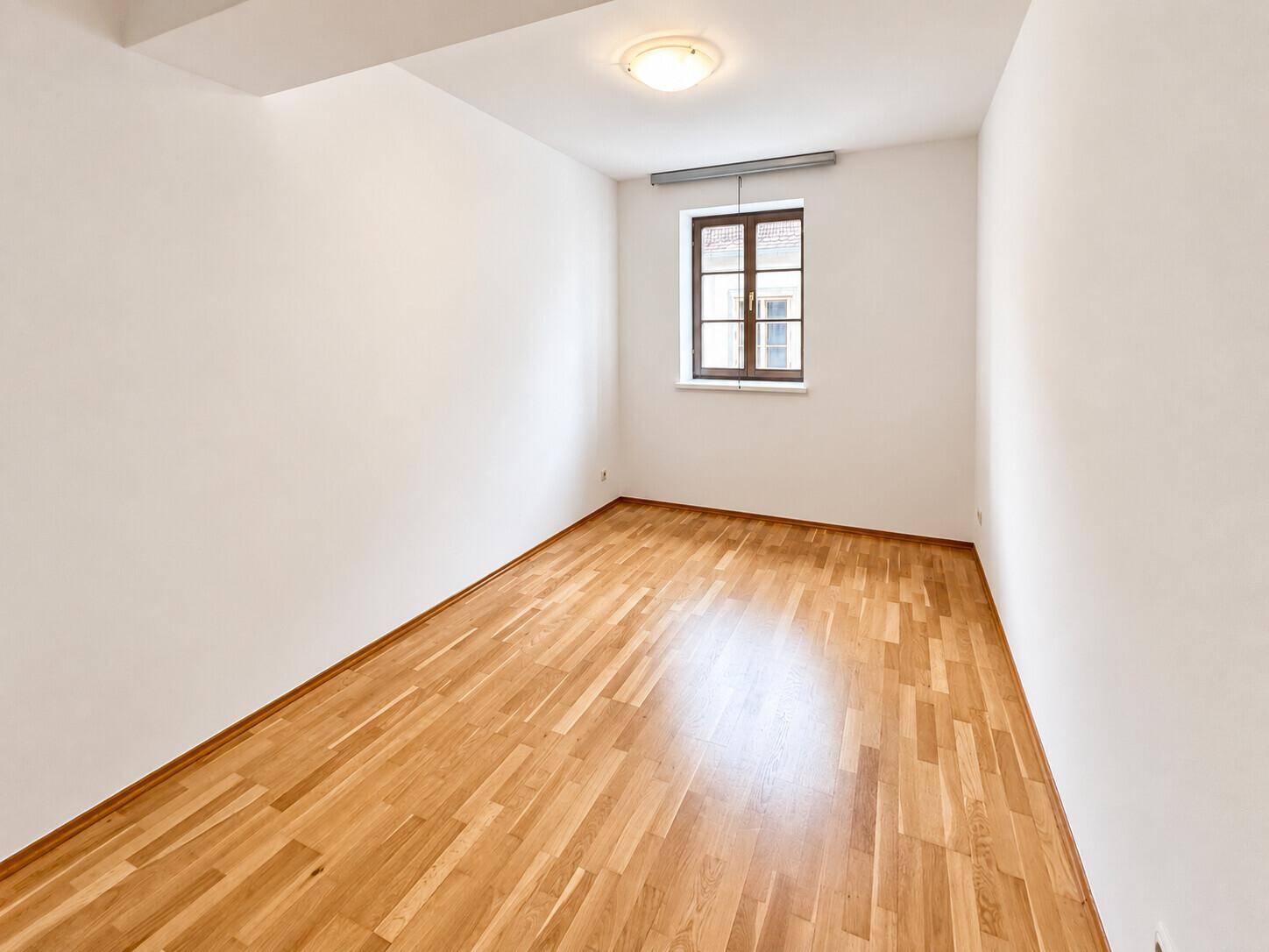 Ruhiges Zimmer mit Parkettboden und einem Fenster, ideal als Schlaf- oder Arbeitszimmer nutzbar.