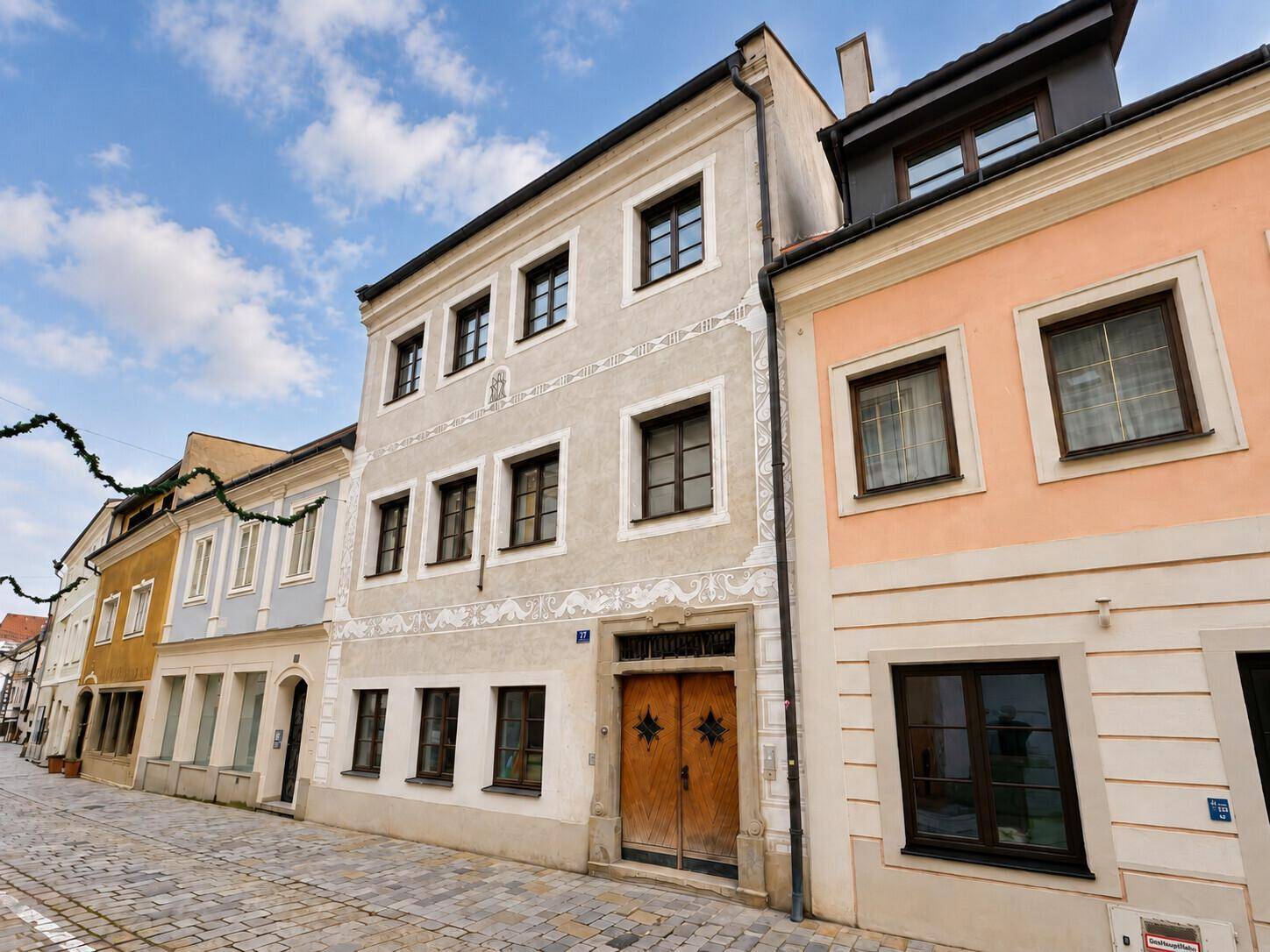 Historisches Gebäude mit verzierter Fassade und Holztür in einer gepflasterten Straße, charmant und gepflegt.