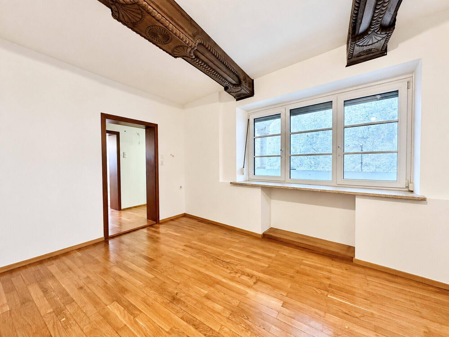Raum mit glänzendem Parkettboden, großen Fenstern und dekorativen Holzbalken an der Decke.
