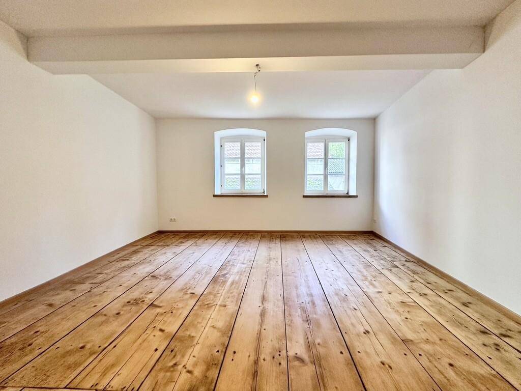 Geräumiger, heller Raum mit rustikalem Holzdielenboden und zwei Fenstern.