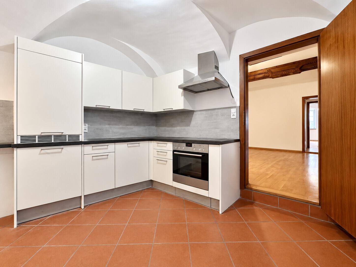Moderne Einbauküche mit weißen Schränken, Terrakottafliesen und Gewölbedecke.
