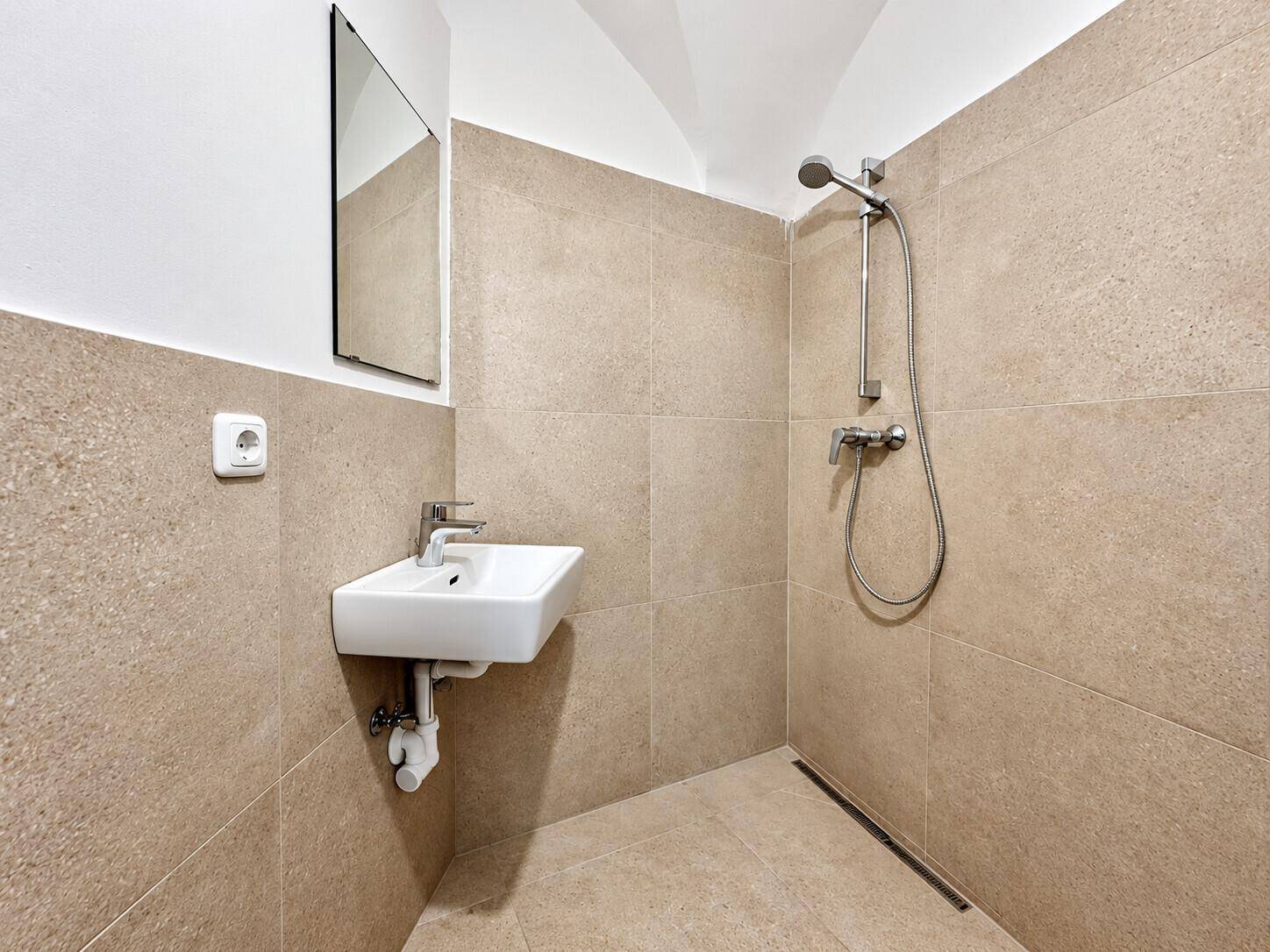 Modernes Badezimmer mit beigefarbenen Fliesen, ebenerdiger Dusche und kleinem Waschbecken.