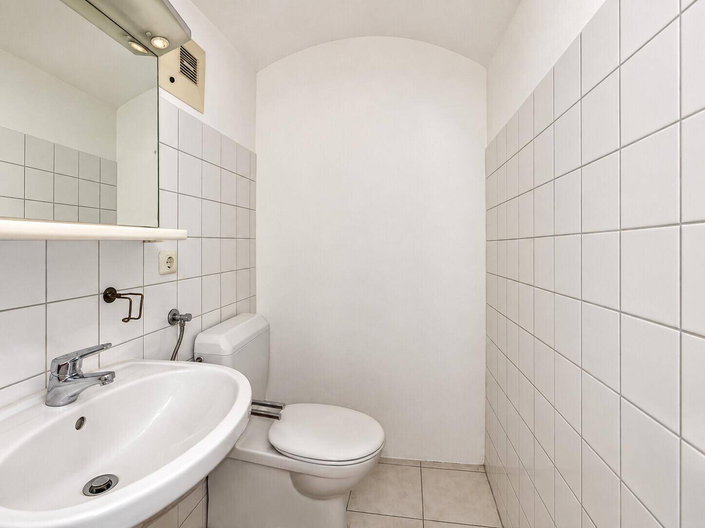 Kleines Gäste-WC mit weißen Fliesen, Waschbecken und Toilette, funktional und hell.