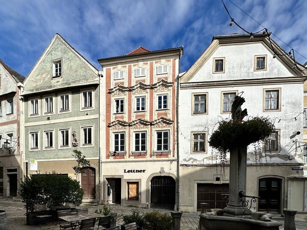 Historische Gebäude an einem Stadtplatz mit Brunnen und Außengastronomie.