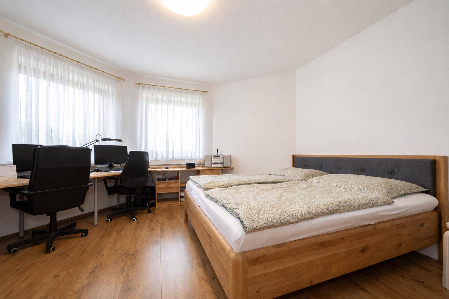 Schlafzimmer mit Doppelbett und integriertem Arbeitsbereich, hell und funktional eingerichtet.