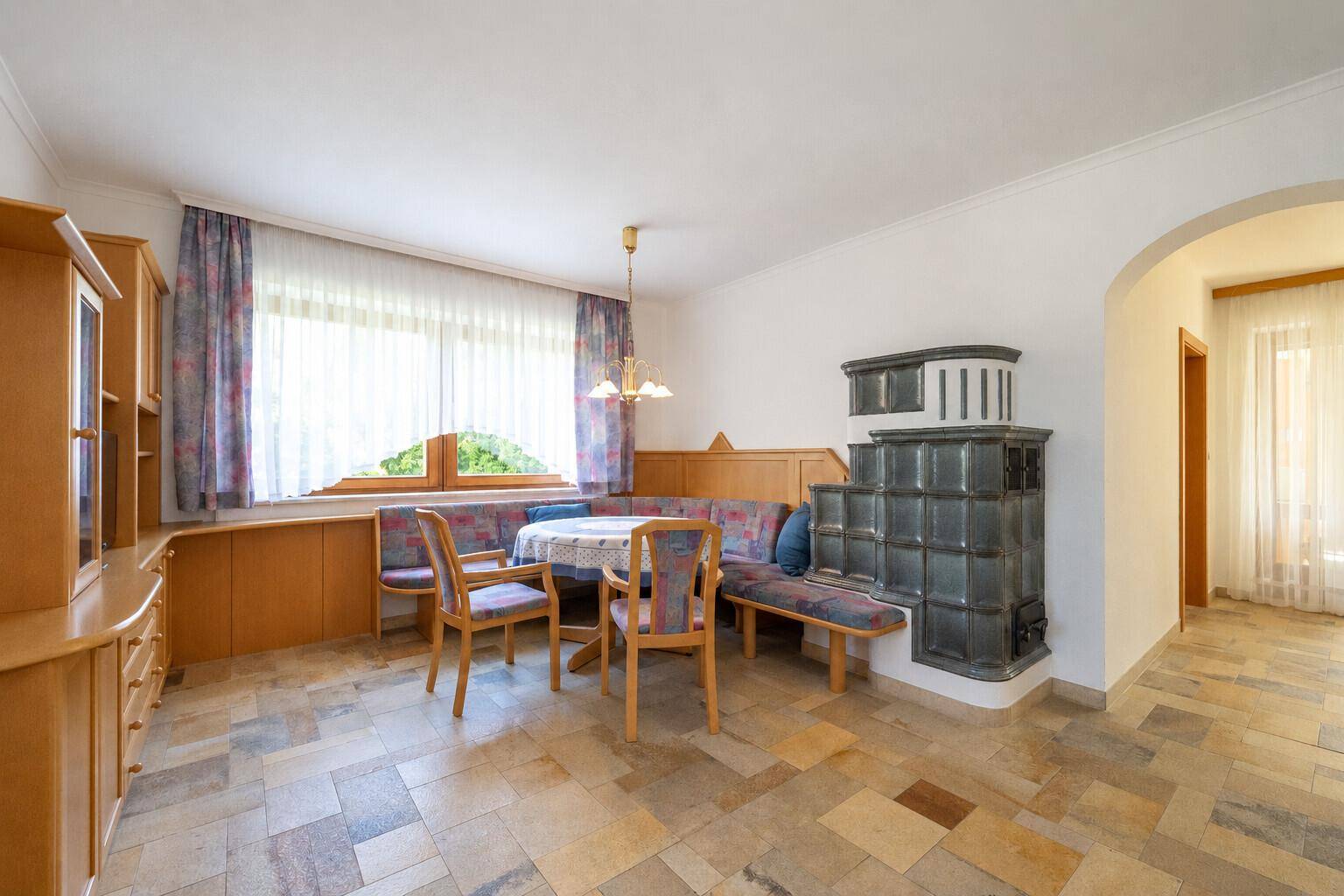 Gemütlicher Essbereich mit traditionellem Kachelofen, Holzbänken und Fliesenboden.